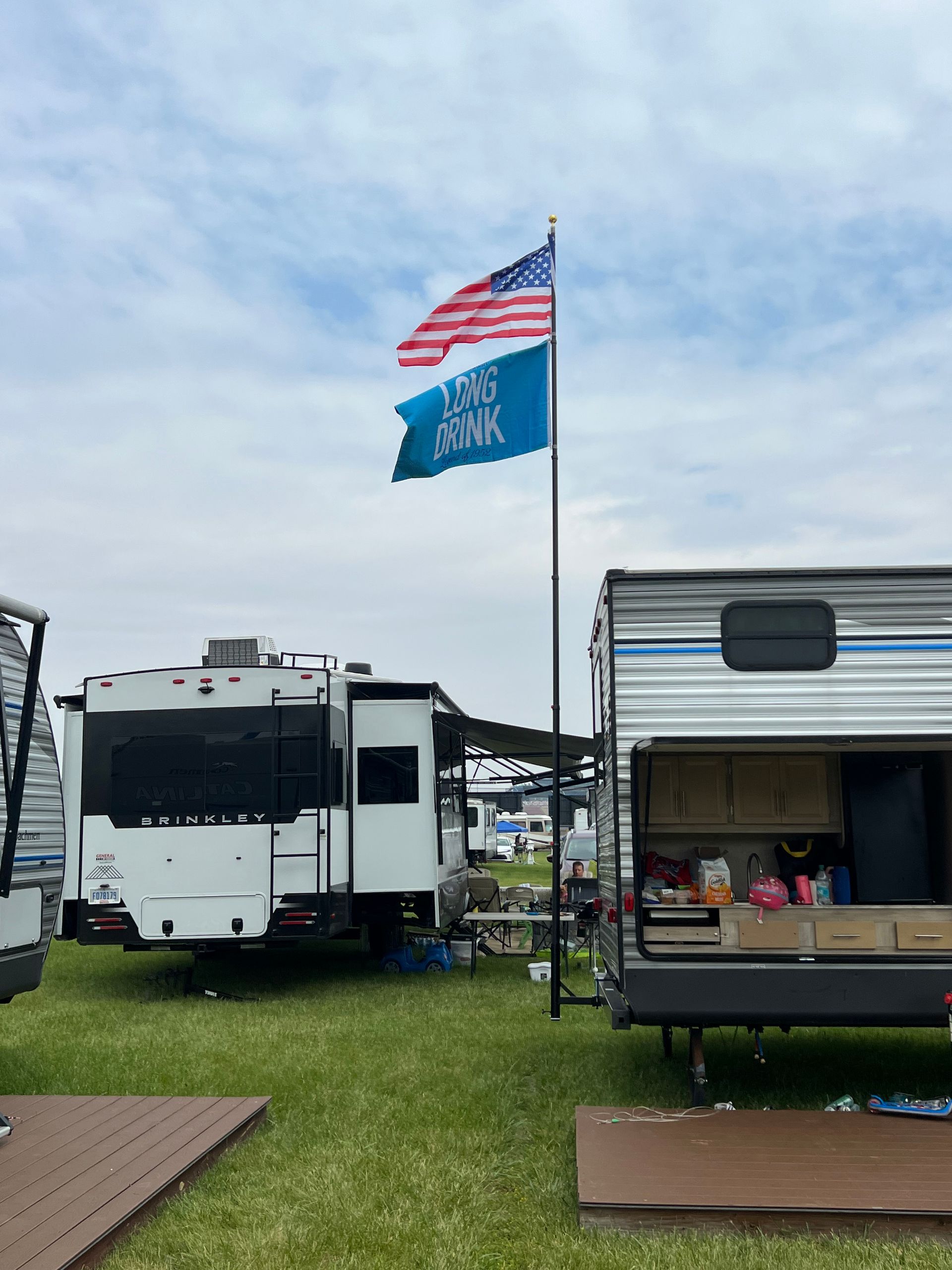 Two RVs with an American flag and blue flag in a grassy campsite on a cloudy day.