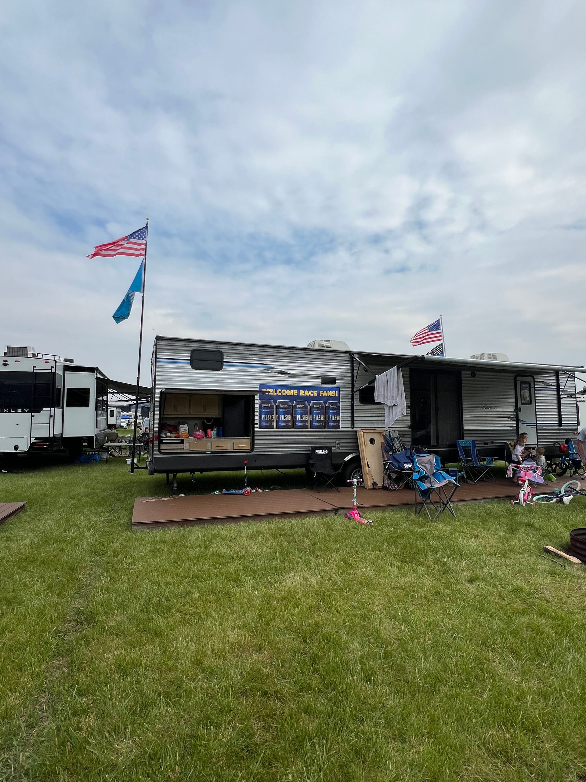 RV with American flags, outdoor seating, and decorations set up on a grassy campsite.