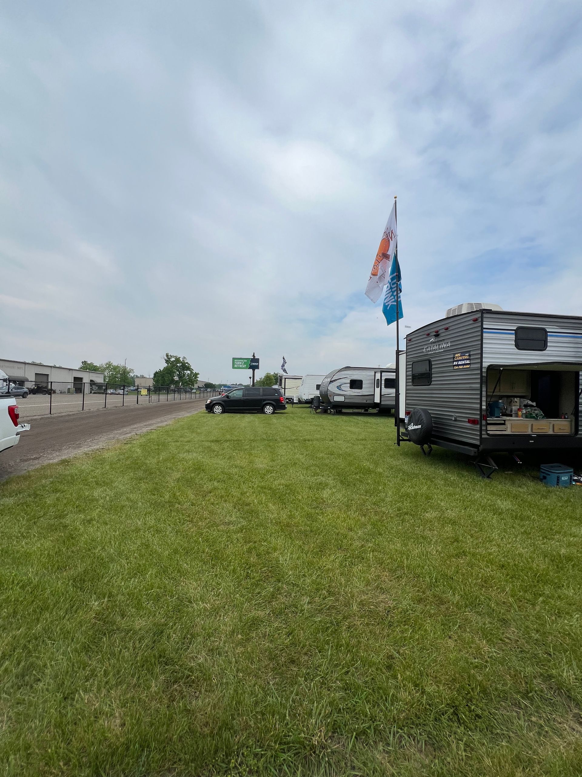 Grassy field with several RVs parked. A flag waves in the wind. Overcast sky.