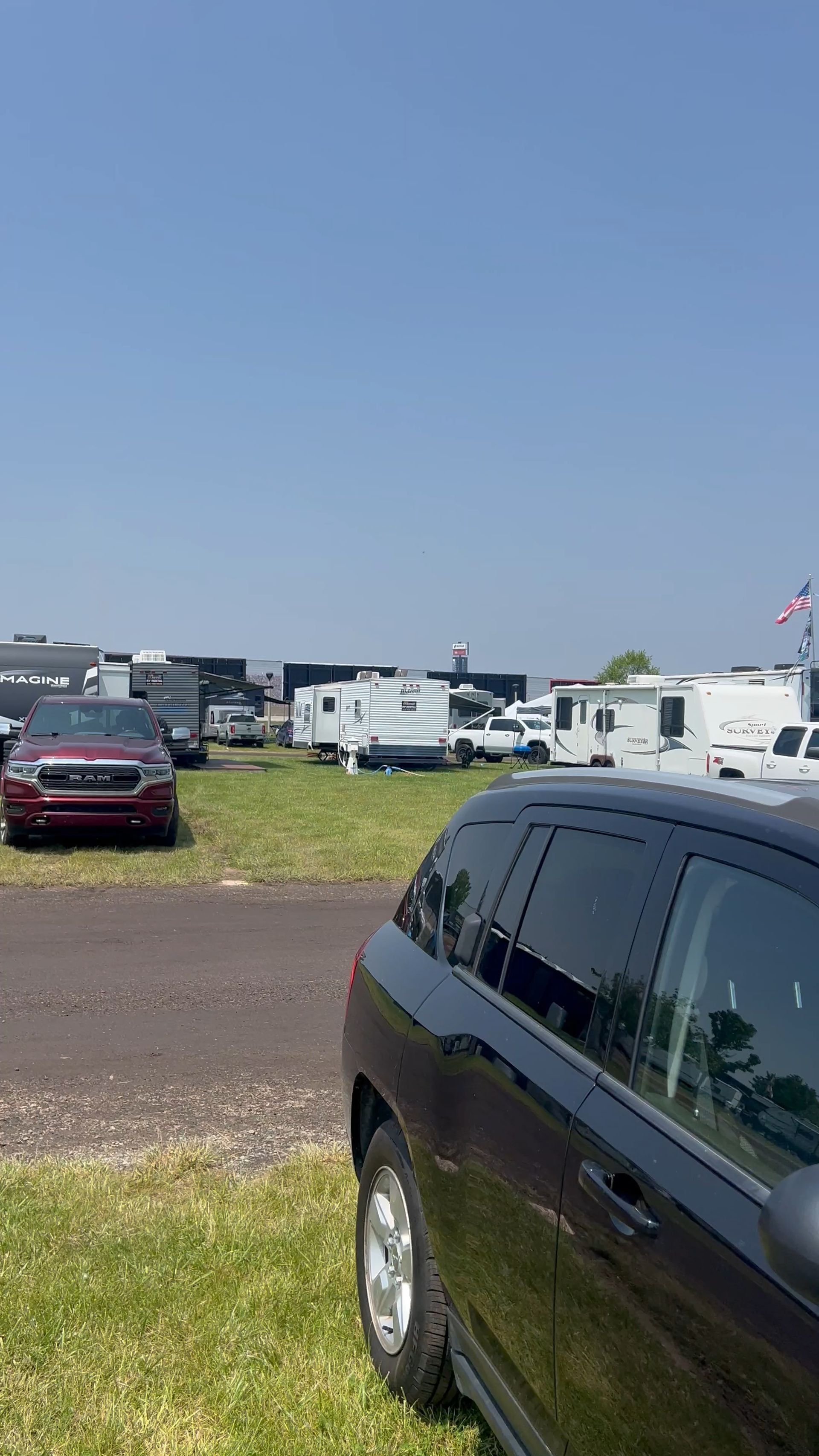 Black SUV parked in a grassy field with RVs and clear blue sky in the background.