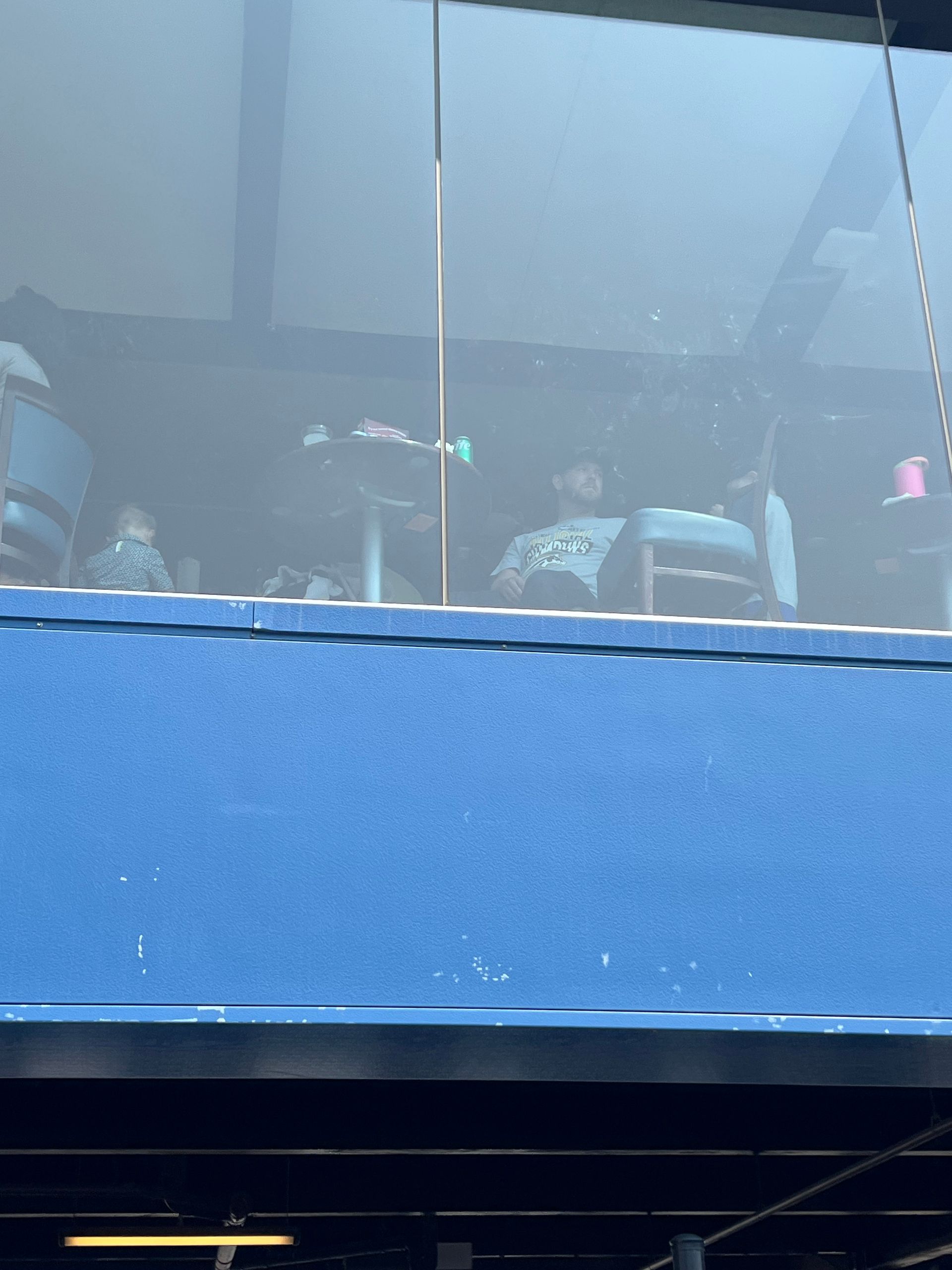 People seated in an enclosed structure with blue exterior, visible through a glass window.