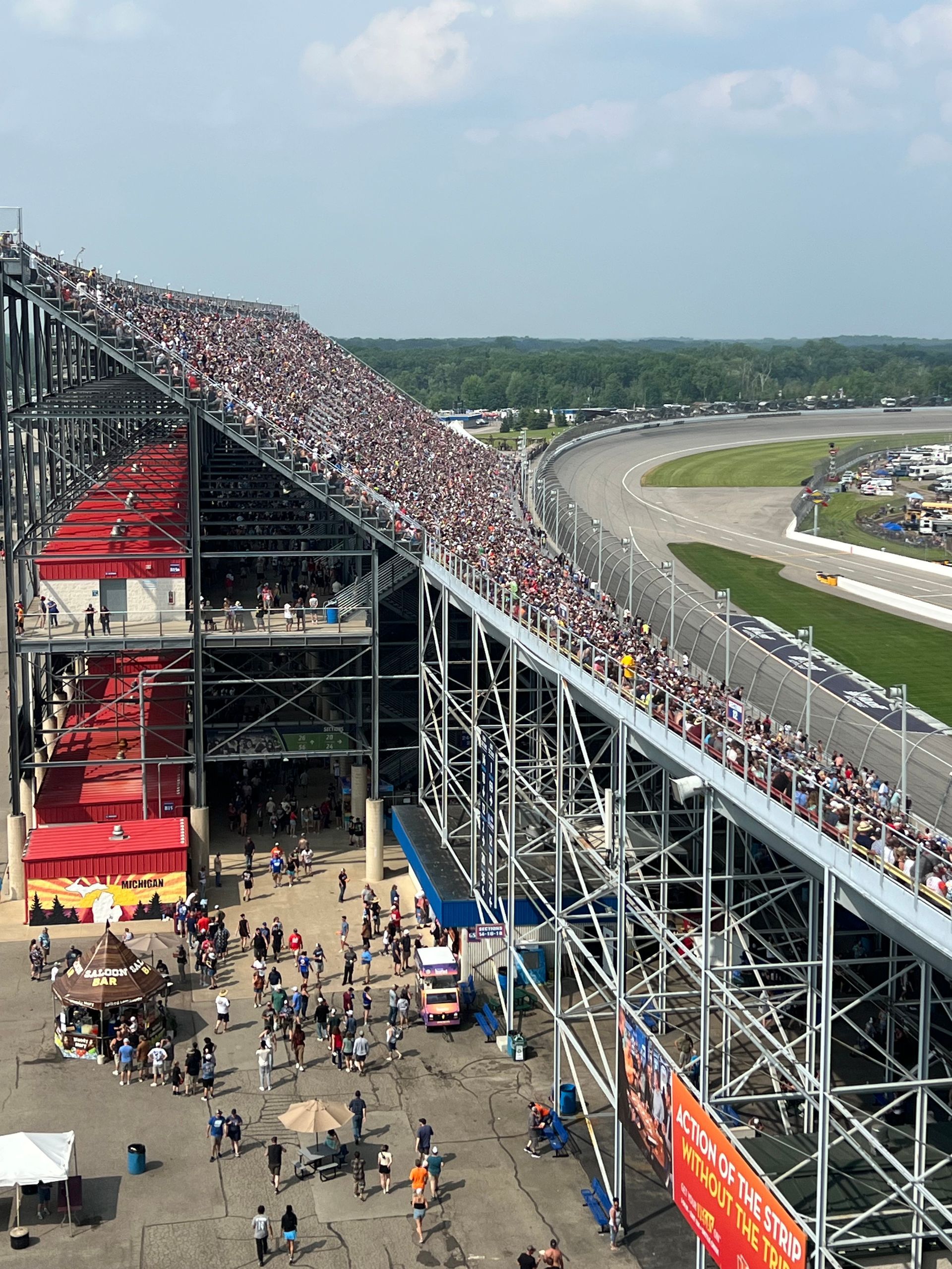 Grandstand packed with people overlooking a racetrack; blue sky, sunny day.