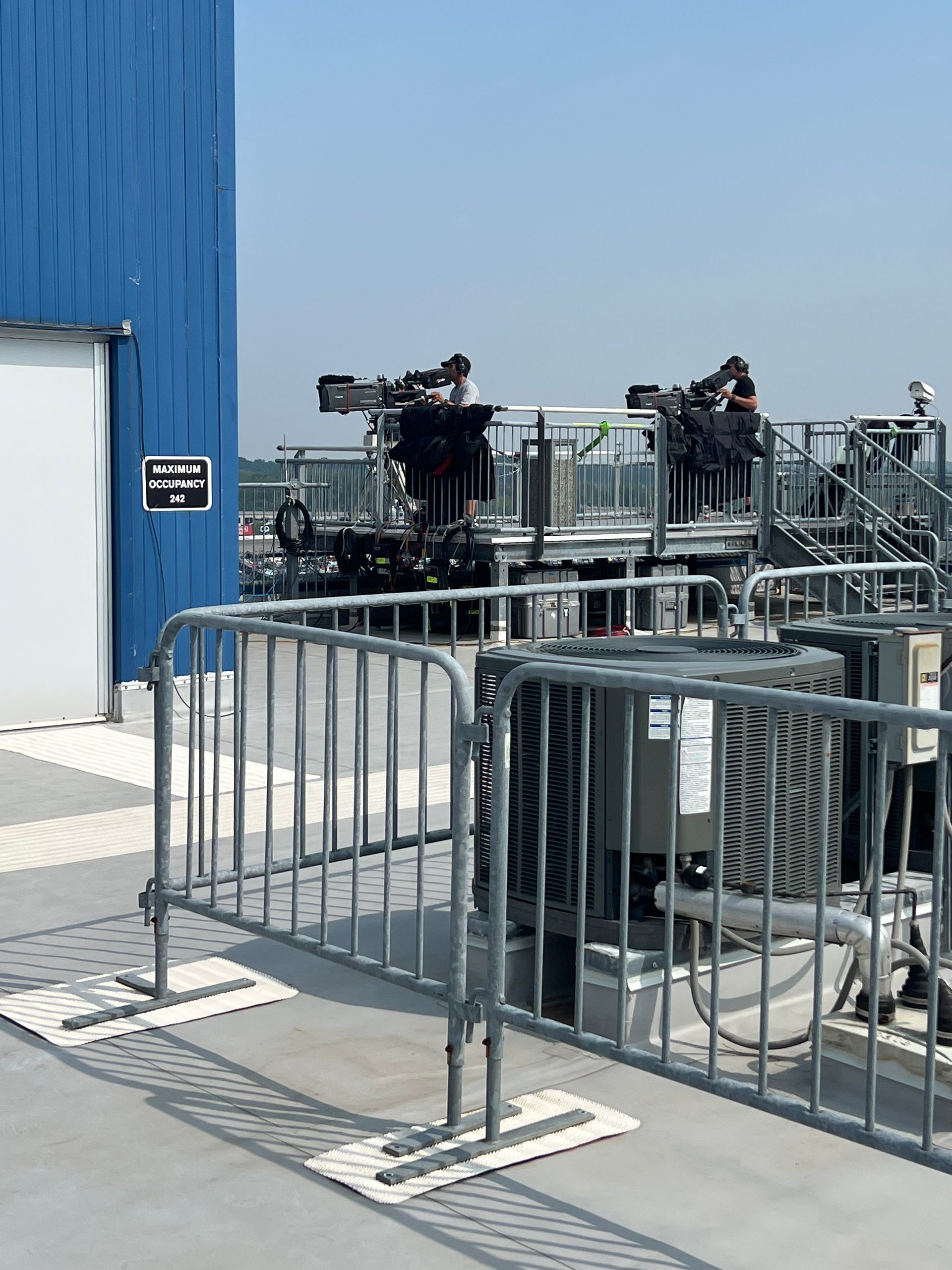 Metal barriers on a rooftop with equipment and a blue building under a clear sky.