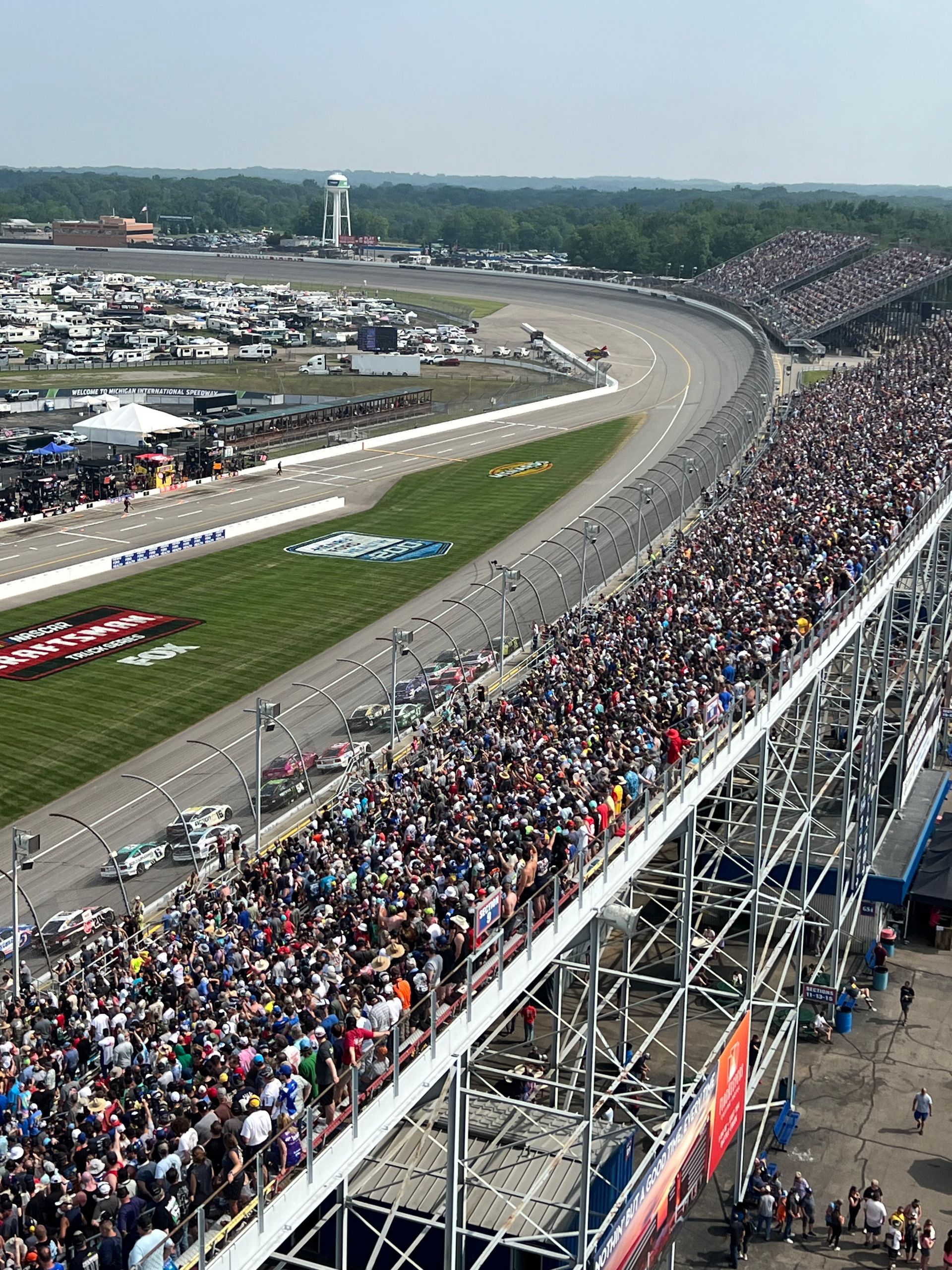 Race track crowded with spectators. Cars speed around track.