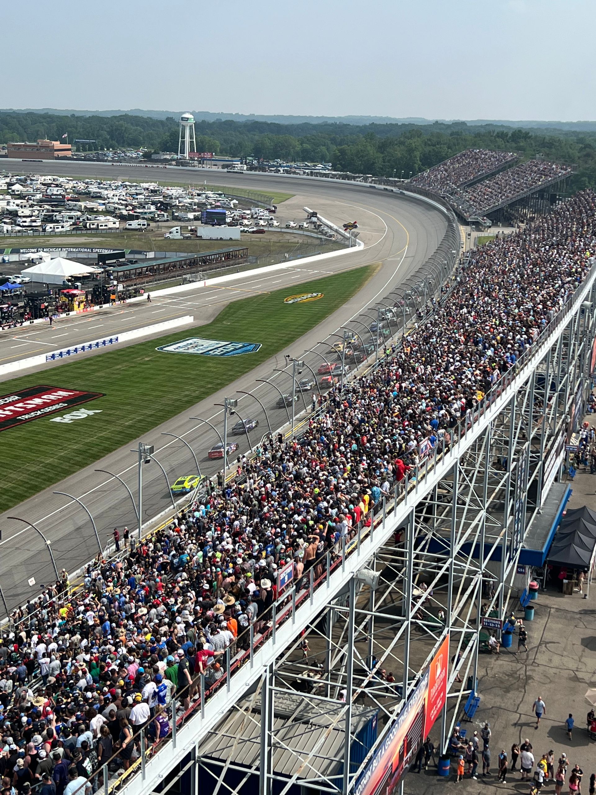 Race track with packed grandstands, cars racing.