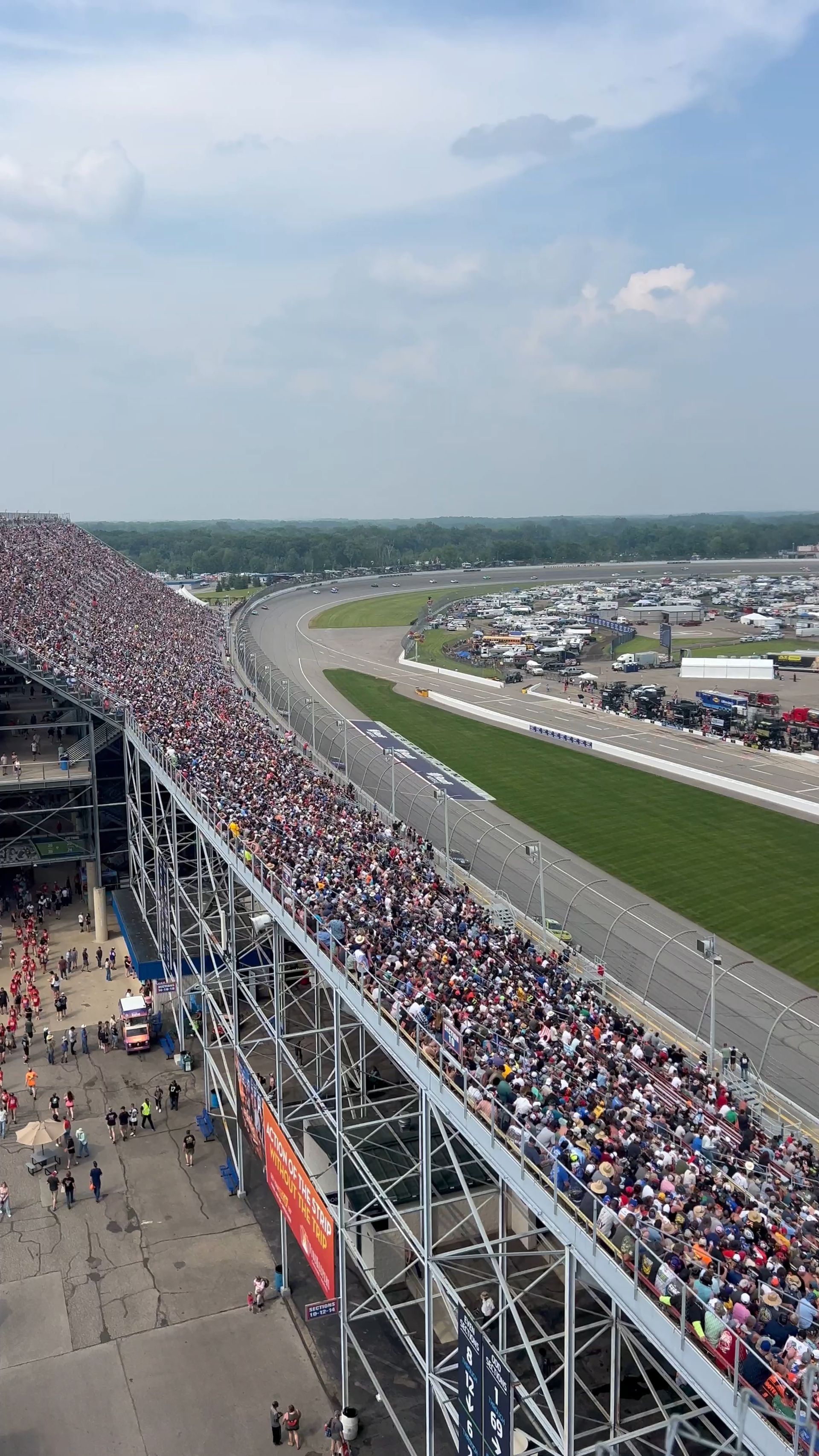 Race track with packed grandstands, blue sky, and parking lots.