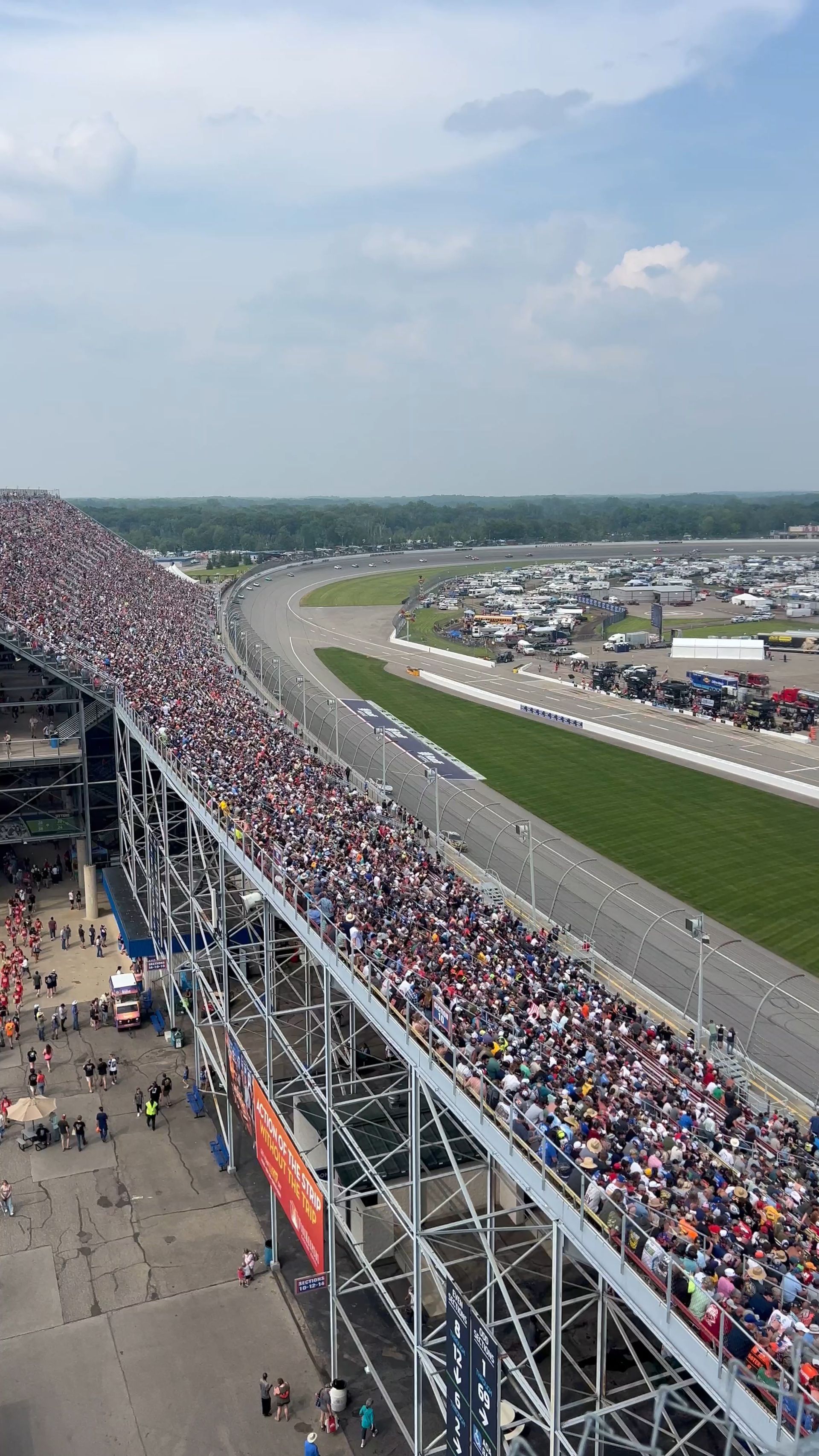 Race track grandstand packed with spectators, cars on the track. Sunny day.