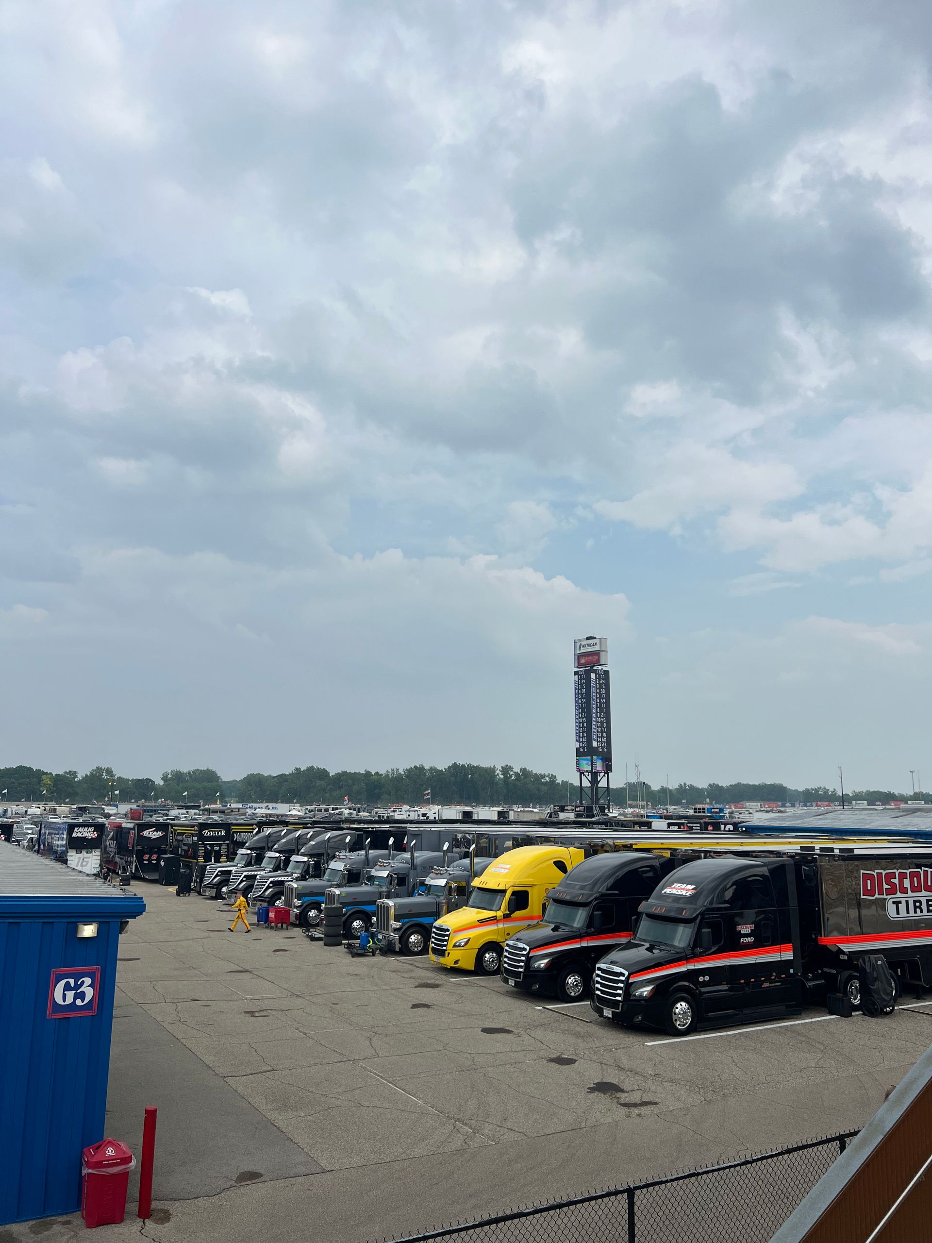Semi-trucks parked at a race track on a cloudy day. A blue box with 