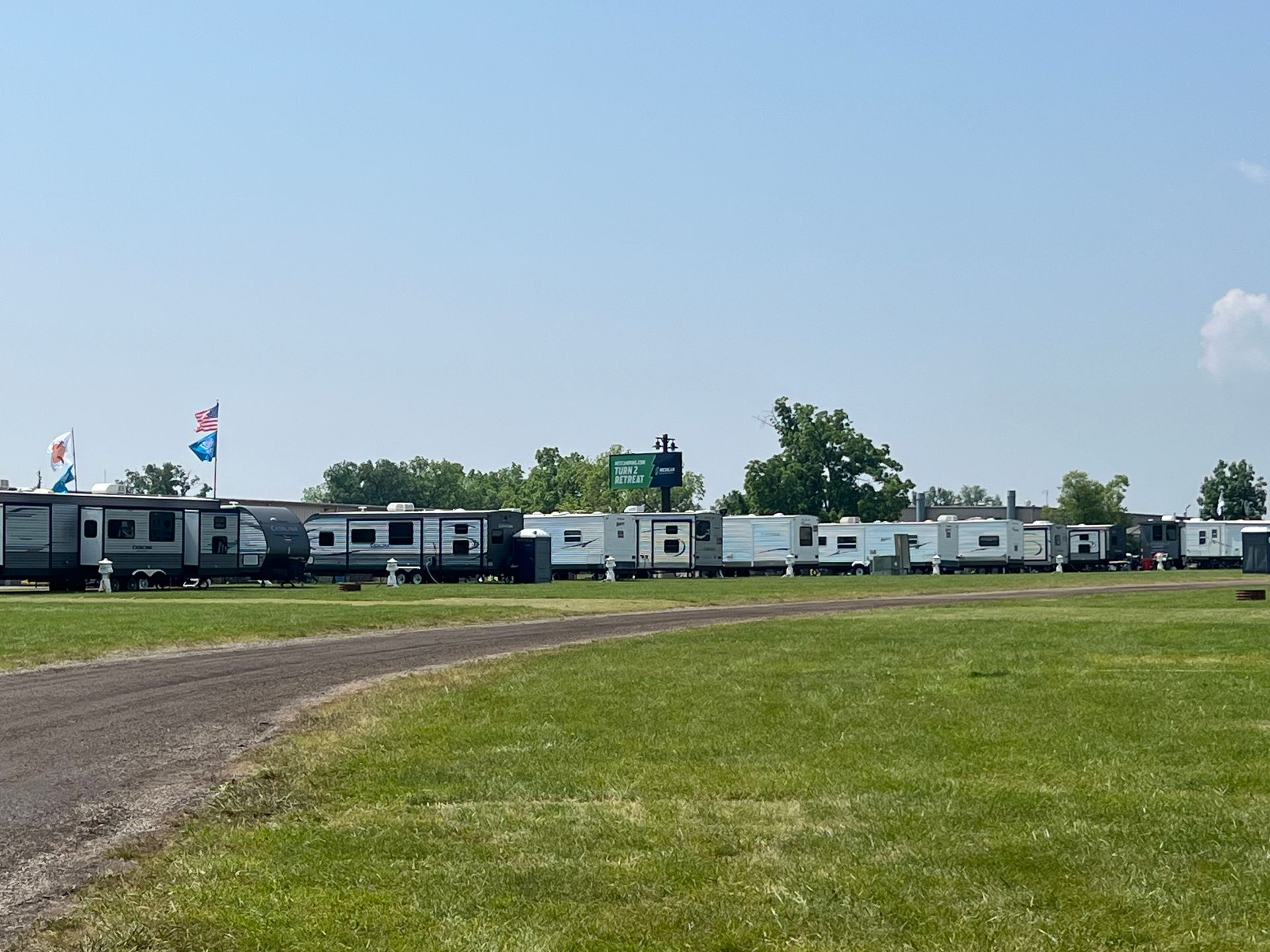 Row of parked RVs on a grassy field under a clear blue sky.