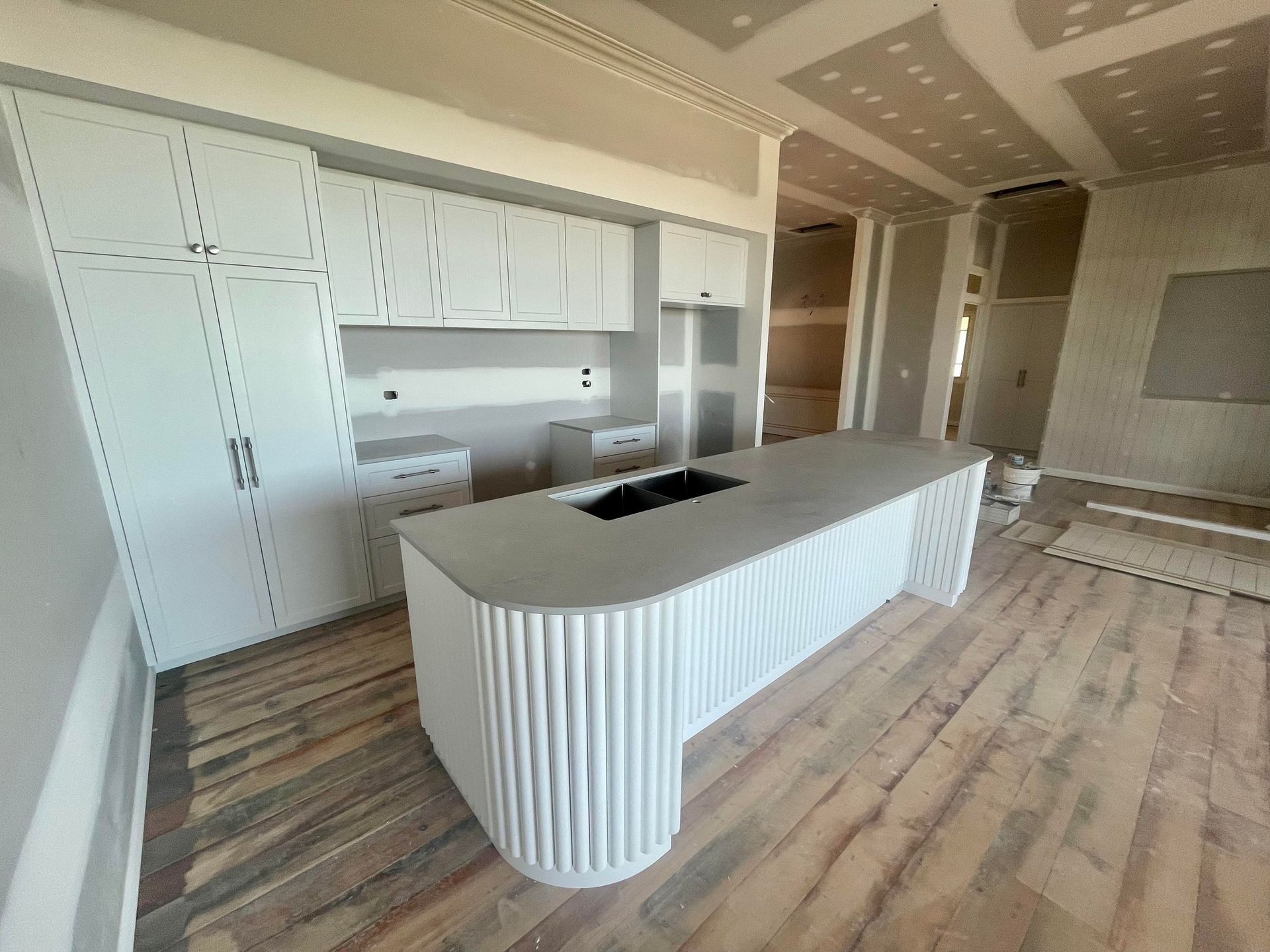 Kitchen in progress with a white fluted-base island, grey countertop, wood-look flooring, and unfinished drywall walls — Jones Building Group in Yeppoon, QLD