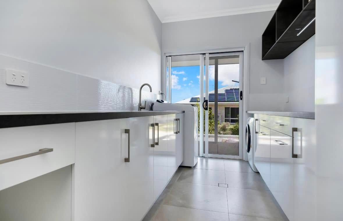 White Laundry Room With Sink, Cabinets, Washer, and Sliding Door to Outdoors — Jones Building Group in Yeppoon, QLD