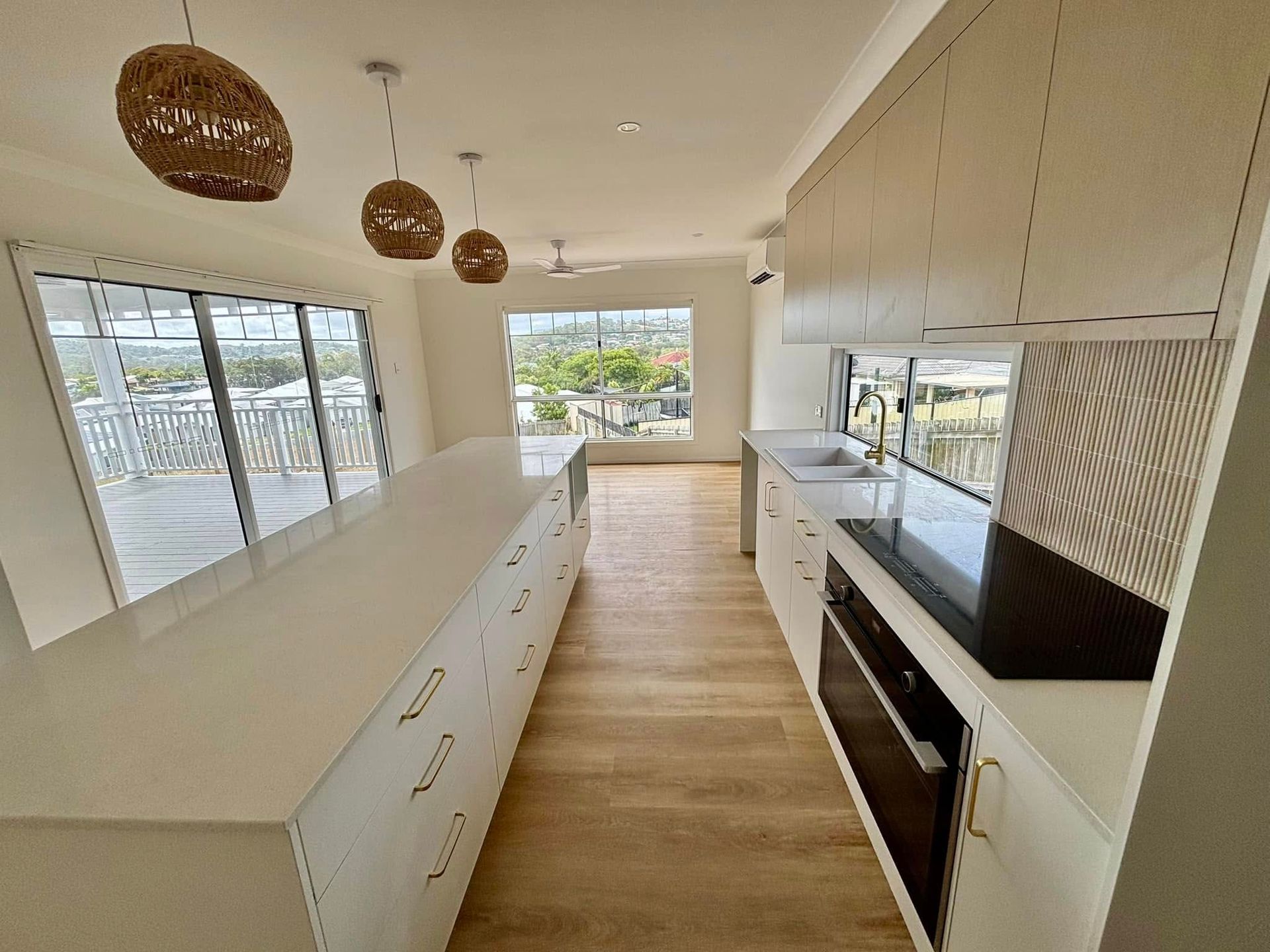 A modern, bright kitchen featuring a long white island, light wood flooring, and minimalist white cabinets.
