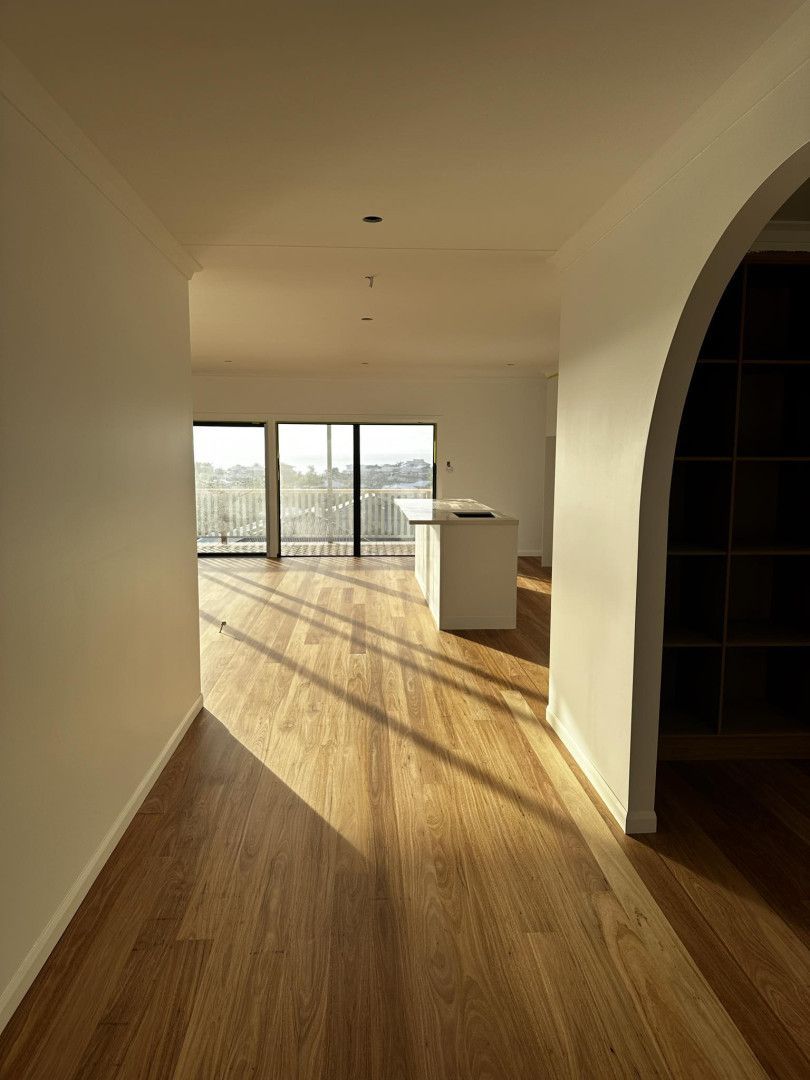 Wooden-floored interior with sunlight streaming in, illuminating a hallway leading to a kitchen with a white island.