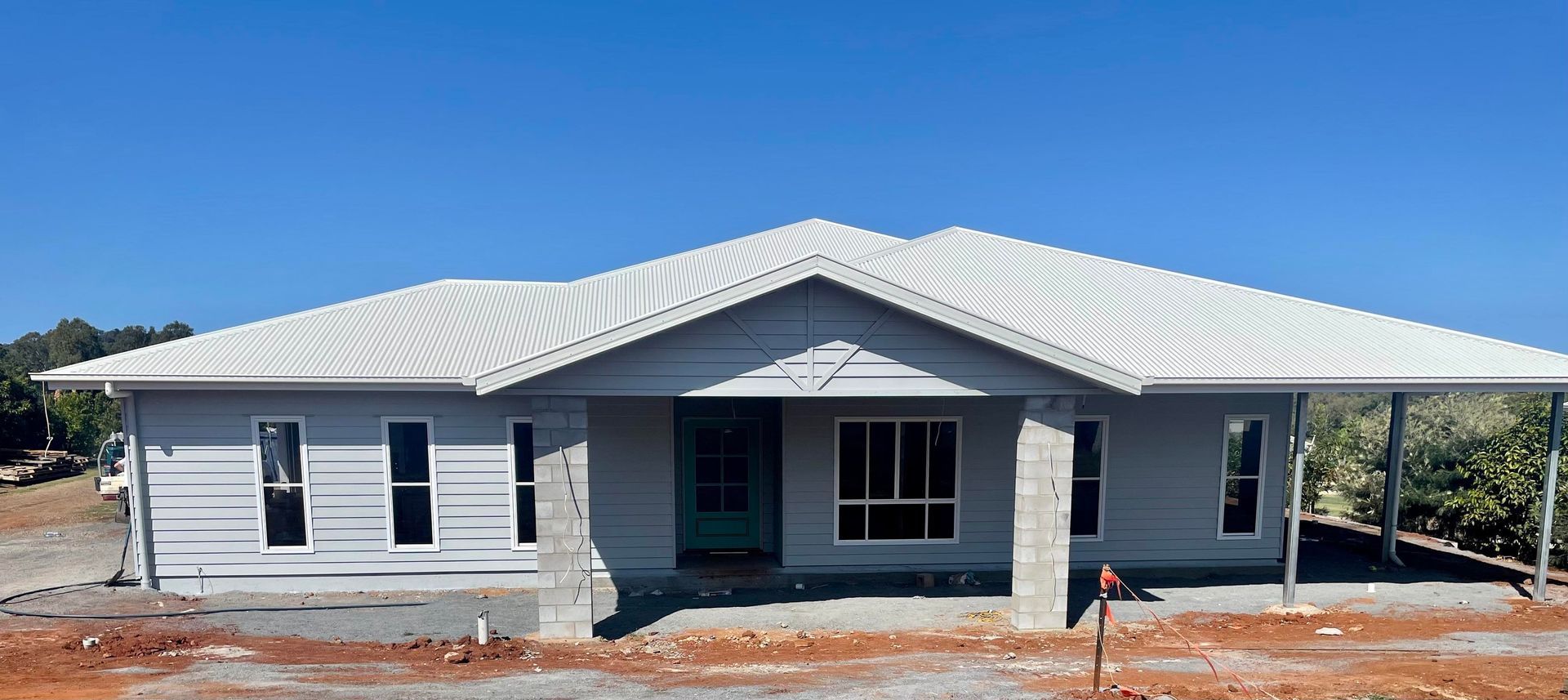 A single-story, light gray house under construction with a white roof and dark-framed windows against a clear blue sky — Jones Building Group in Yeppoon, QLD