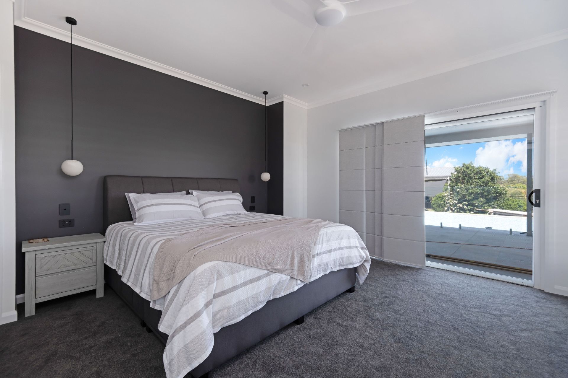 A modern bedroom with a dark gray accent wall, a plush bed with striped bedding, and a sliding door leading to a balcony.