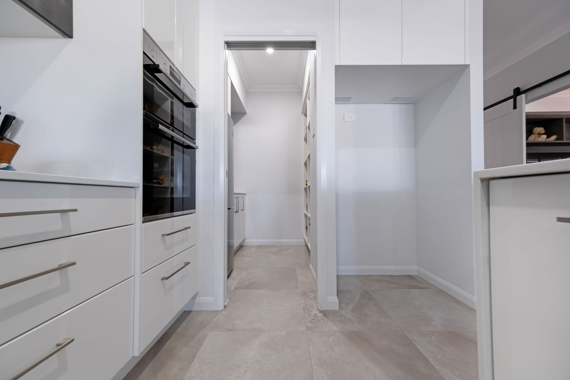A modern, all-white kitchen with a double wall oven, cabinetry, and a walk-in pantry area with light tile flooring — Jones Building Group in Yeppoon, QLD