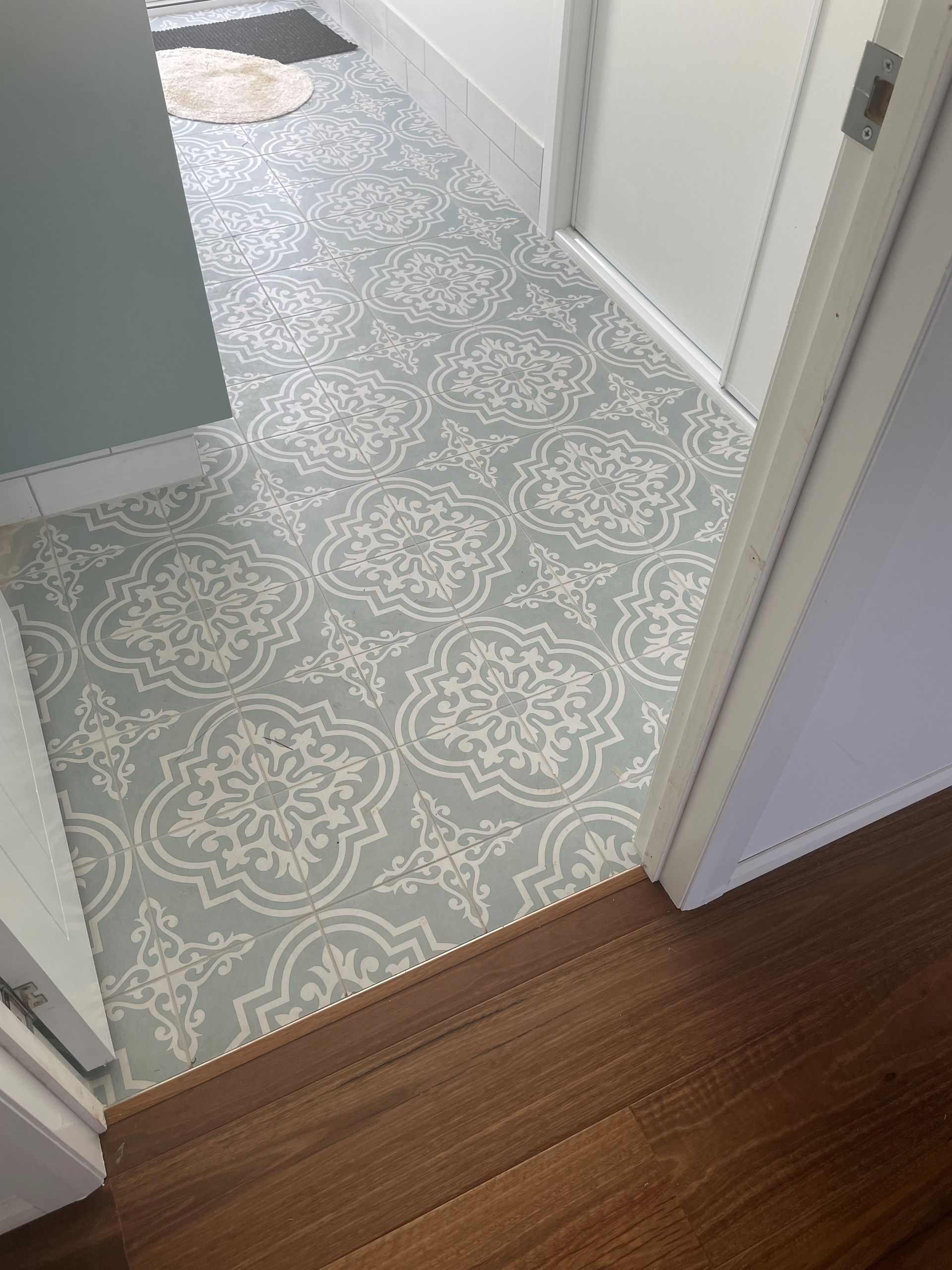 A high-angle shot shows a hallway with light-blue and white patterned floor tiles transitioning to dark wood flooring — Jones Building Group in Yeppoon, QLD