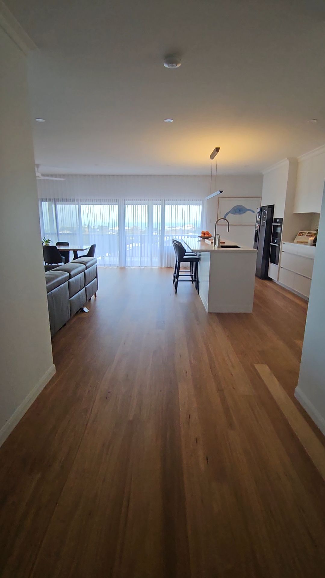 A view down a hallway into an open-plan kitchen and living area with light wood flooring and large windows — Jones Building Group in Yeppoon, QLD