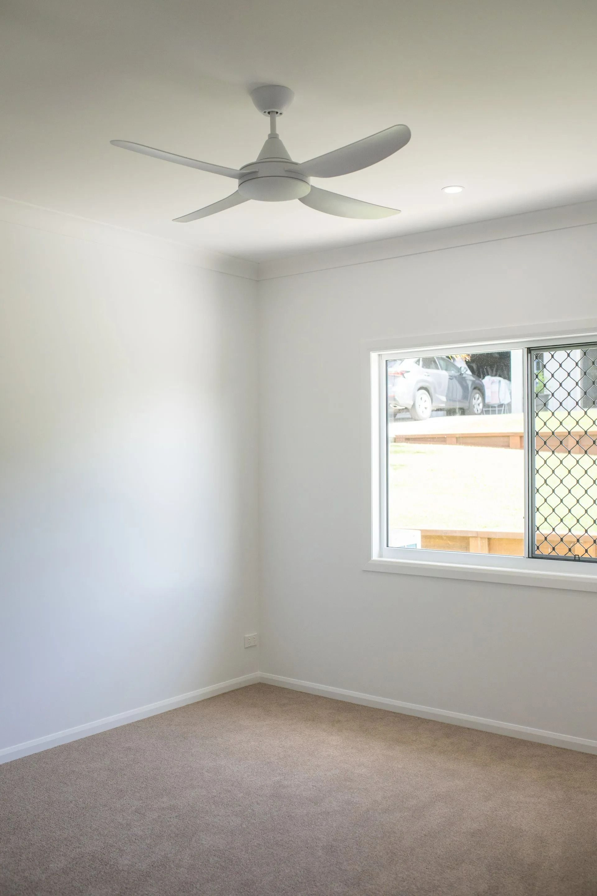 Empty White Room With Ceiling Fan, Window, and Beige Carpet — Jones Building Group in Yeppoon, QLD