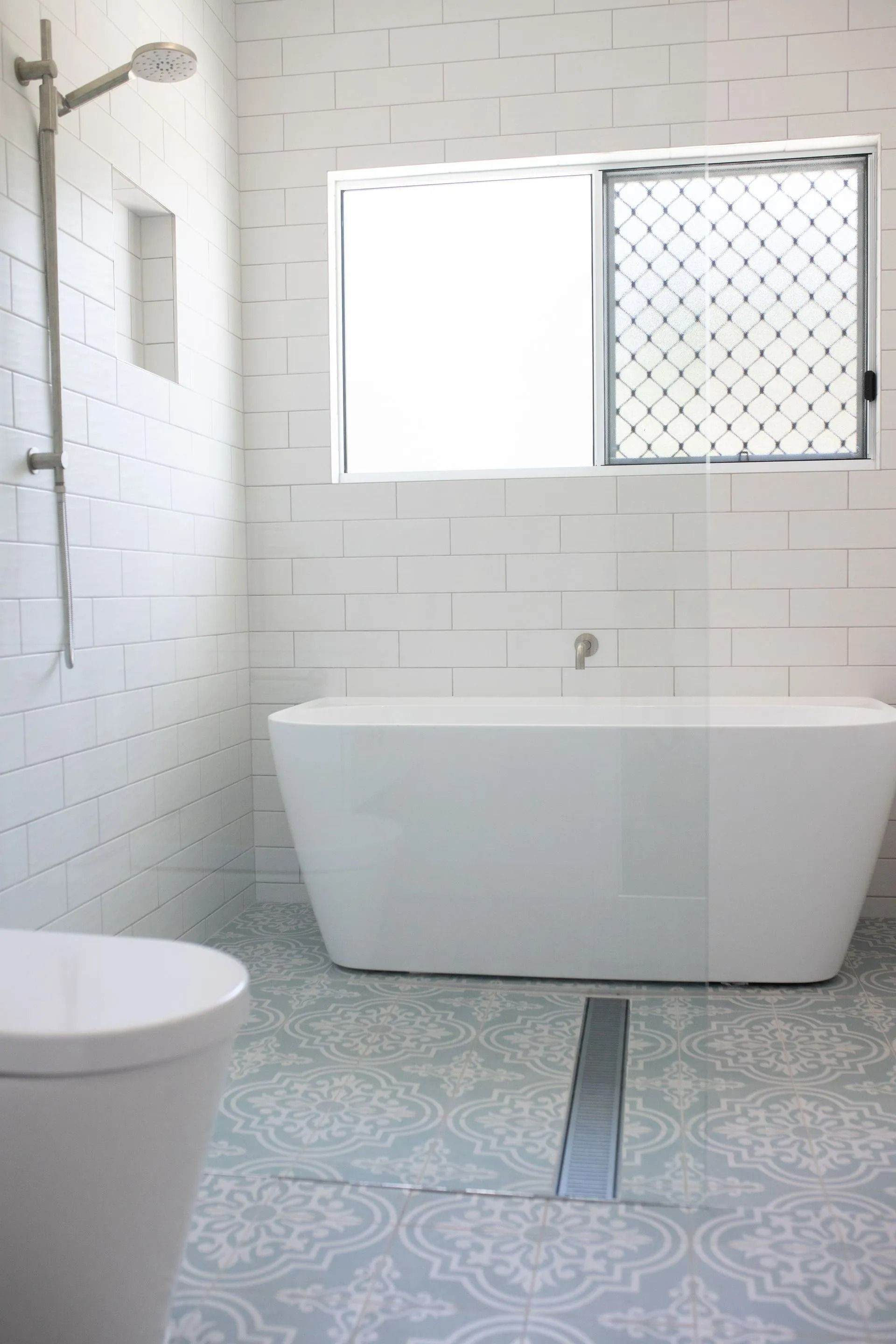 White Bathroom With Freestanding Tub, Shower, Window, and Patterned Tile Floor — Jones Building Group in Yeppoon, QLD