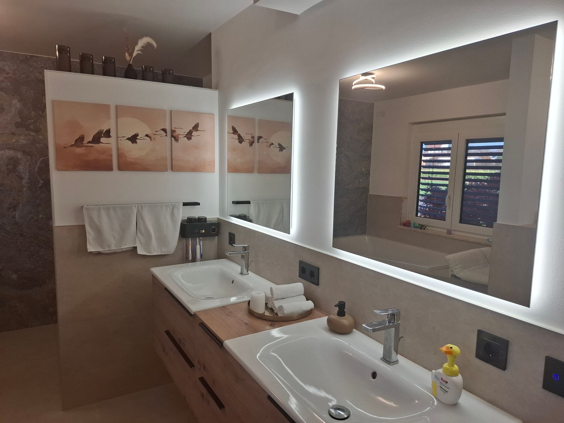 Modernes Badezimmer mit Doppelwaschbecken, großen Spiegeln und dekorativer Kunst.
