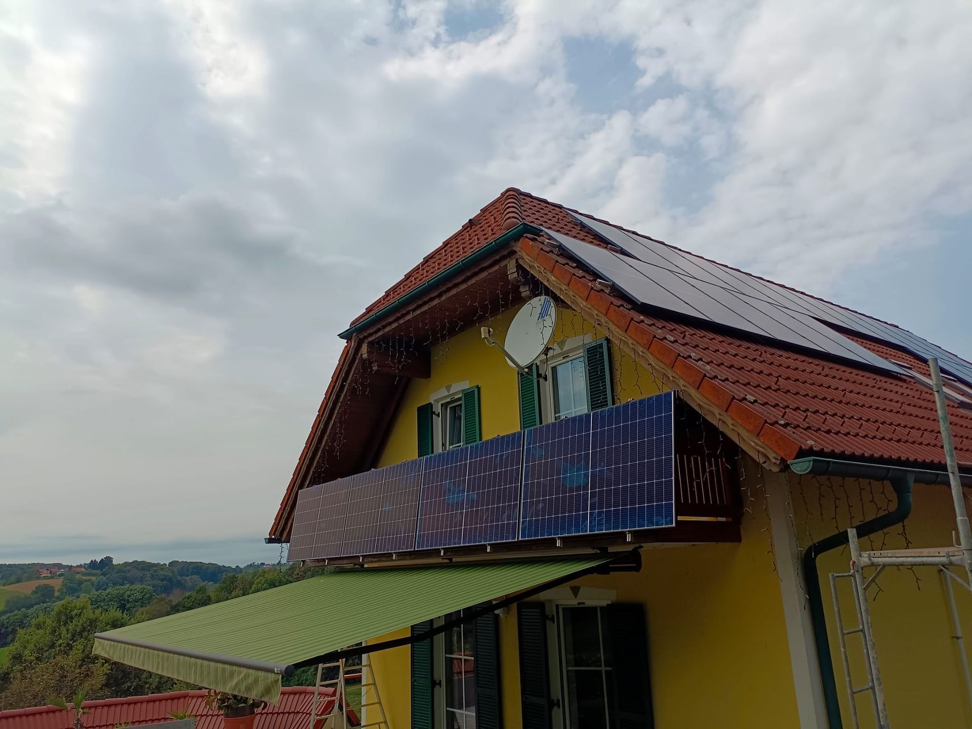 Ein gelbes Haus mit einer grünen Markise und Solarzellen auf dem Dach.