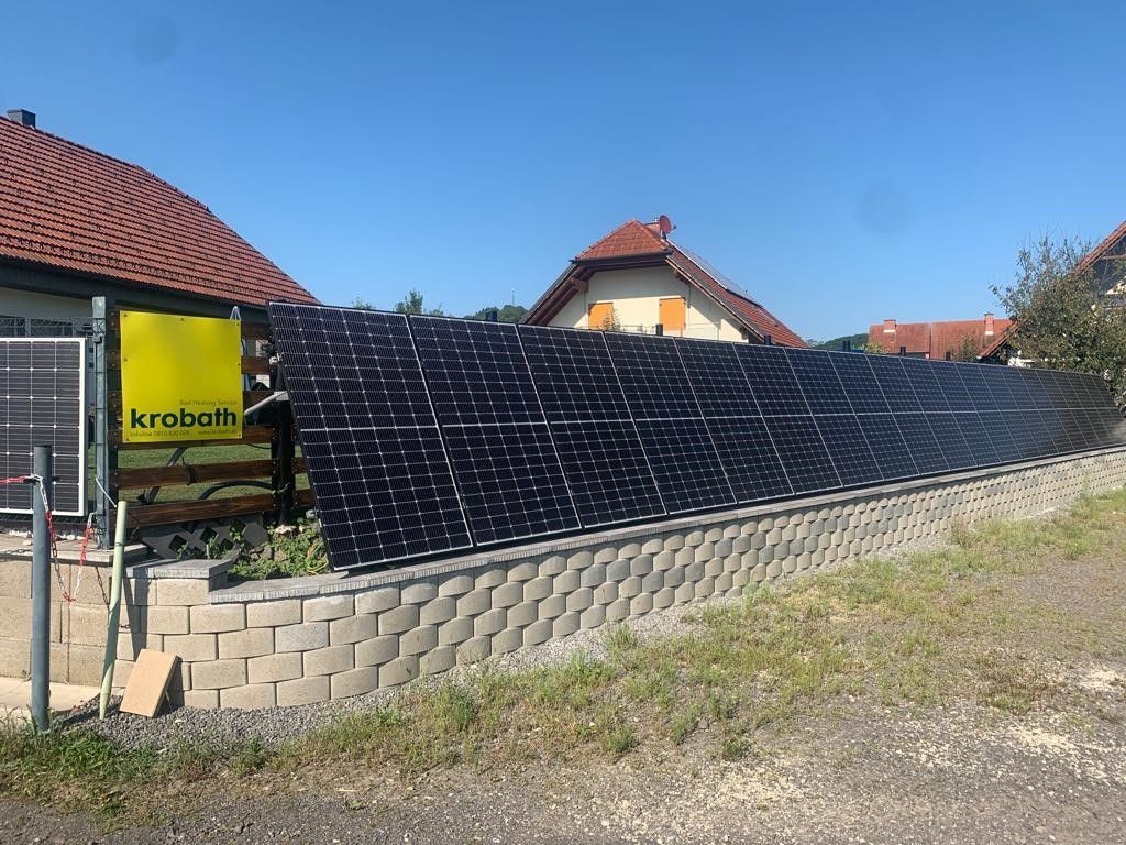 Ein Zaun mit vielen Solarmodulen vor einem Haus.