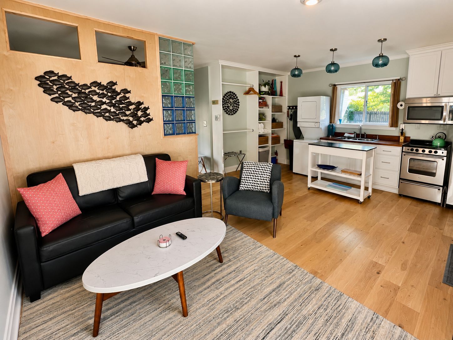 Modern living room with black sofa, pink pillows, white coffee table, and open kitchen in the background