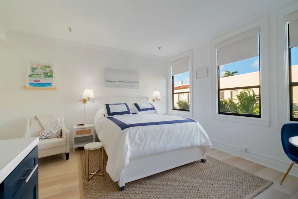 A bedroom with a bed , chair , table and two windows.