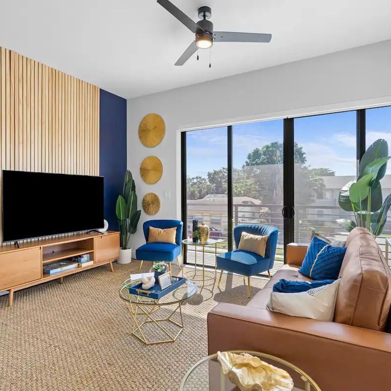 A living room with a couch , chairs , a flat screen tv and a ceiling fan.