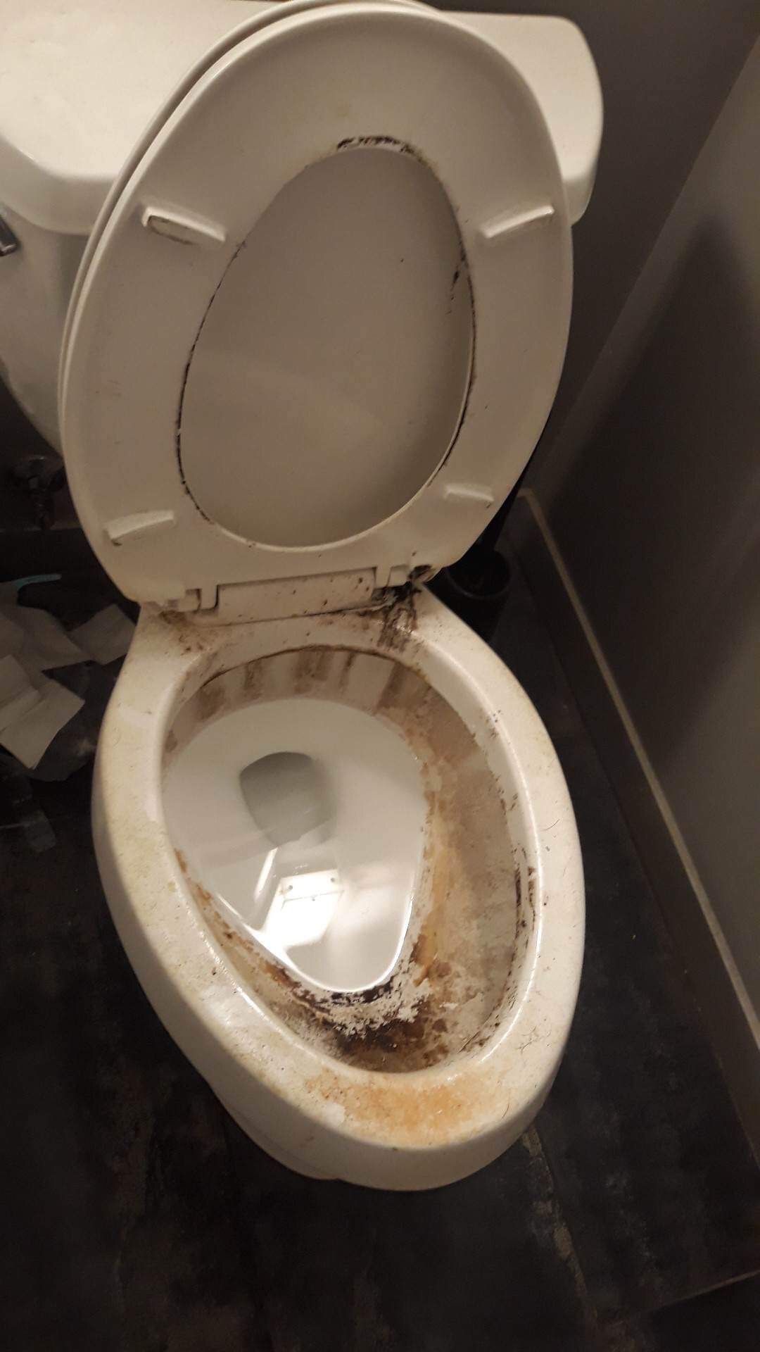 A dirty toilet with the lid open in a bathroom.