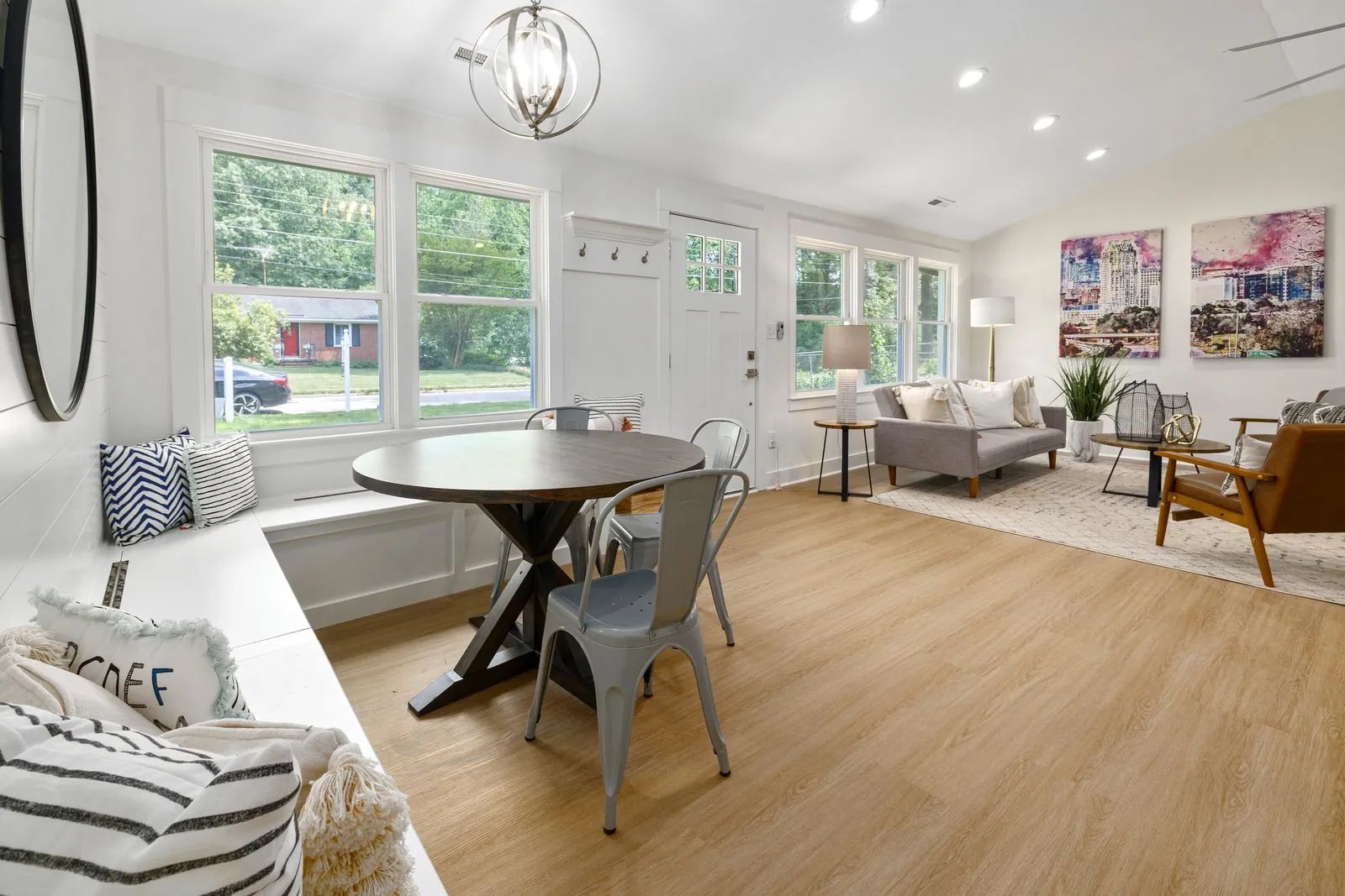 Bright modern living room with white walls, wood floors, gray furniture, and large windows with natural light