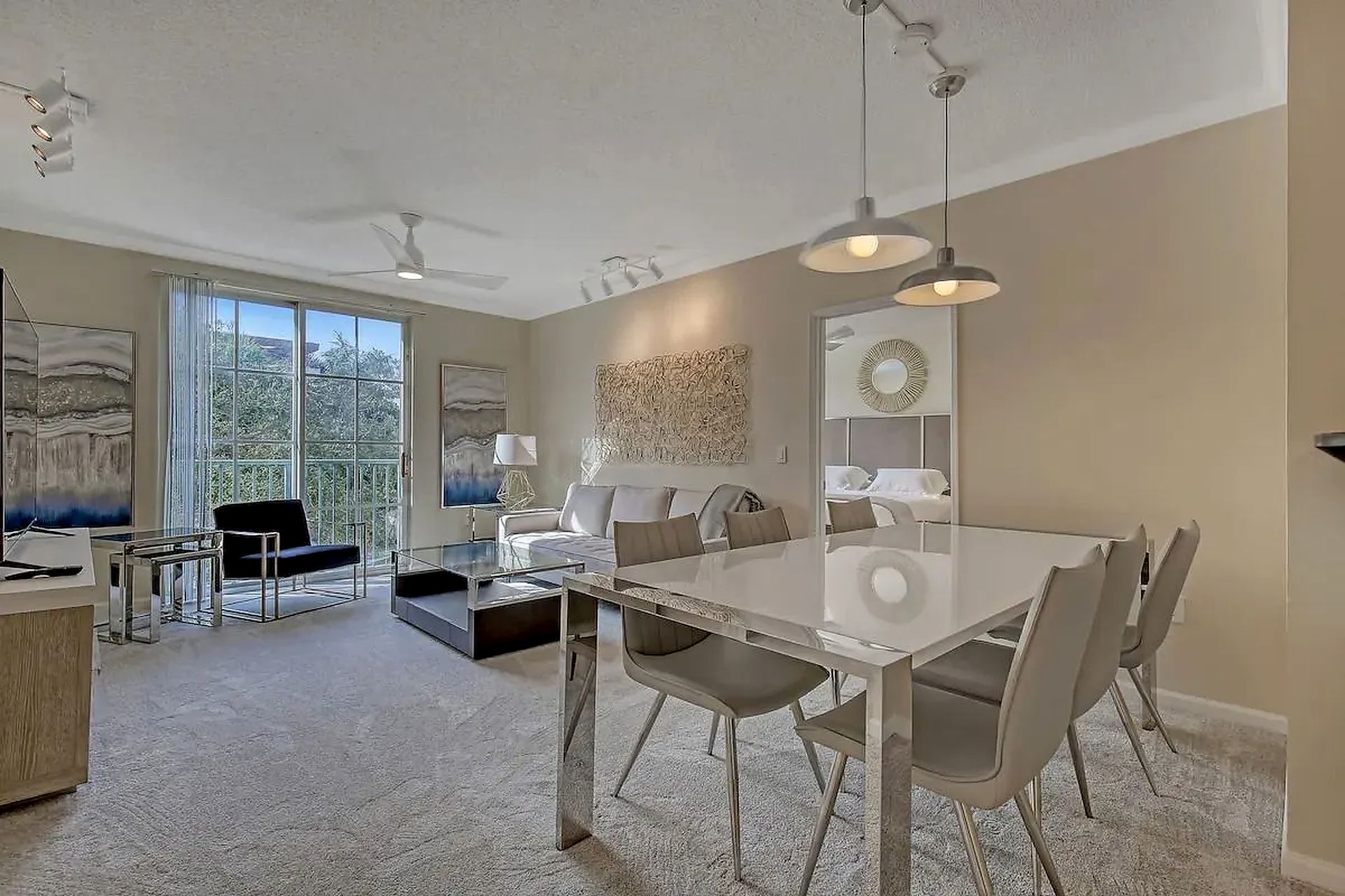 Modern open-plan dining and living room with beige decor, glass table, sofa, and balcony doors