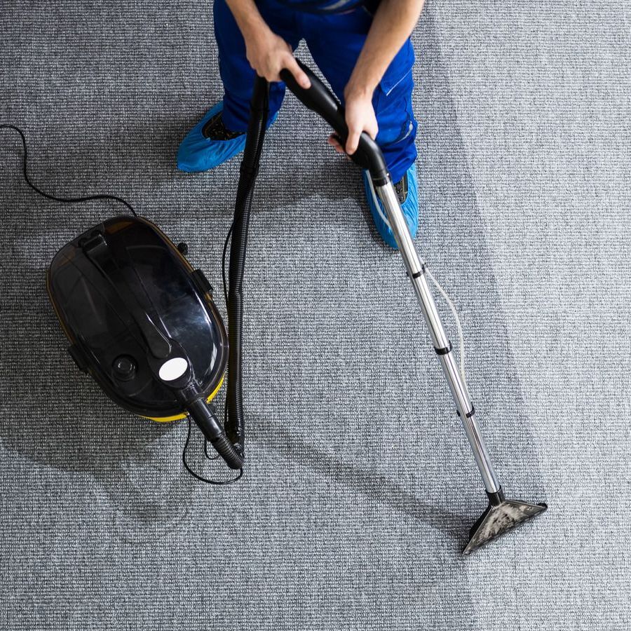 Person vacuuming gray carpet with a black vacuum, creating a cleaned strip.