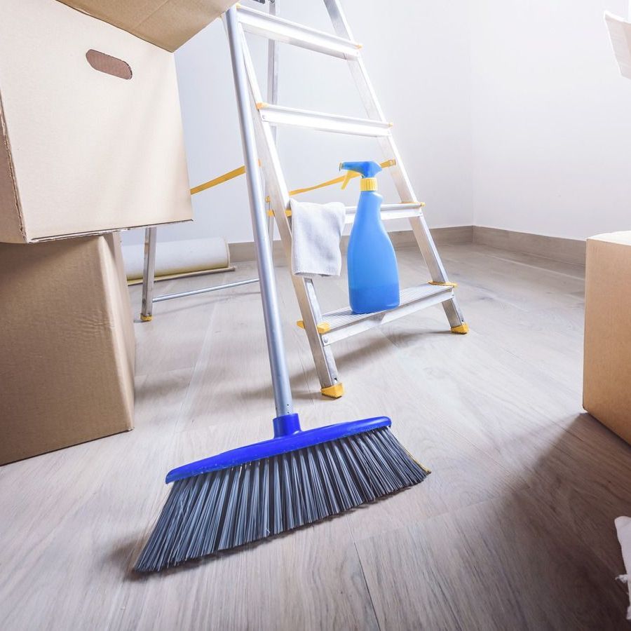 A blue broom is sitting on a wooden floor next to a ladder.