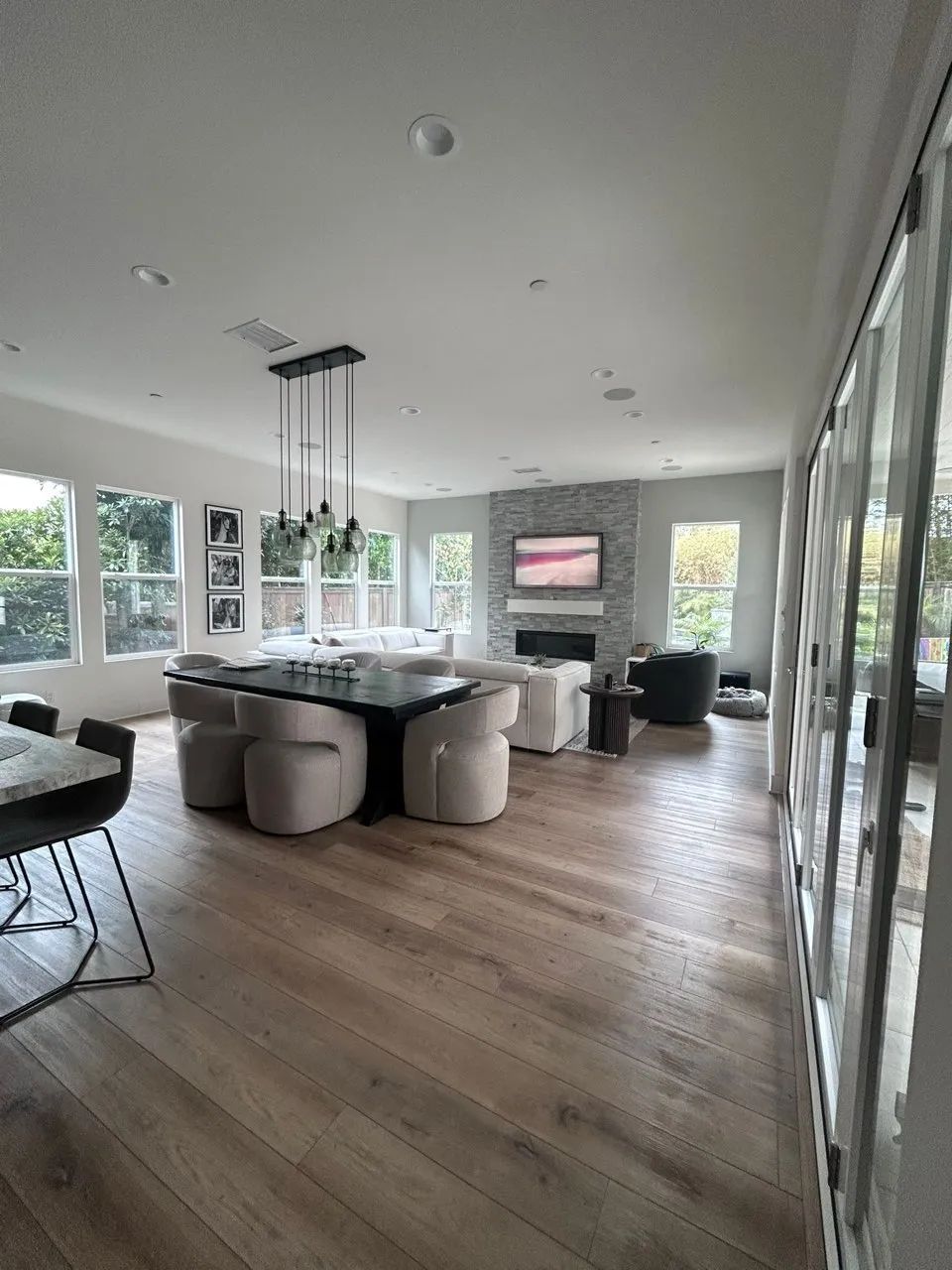 Modern open-plan living room with large windows, gray sofa, kitchen island, and wood floors
