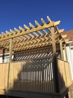 A wooden pergola structure attached to the side of a house with vertical slat privacy screening and a slatted roof.
