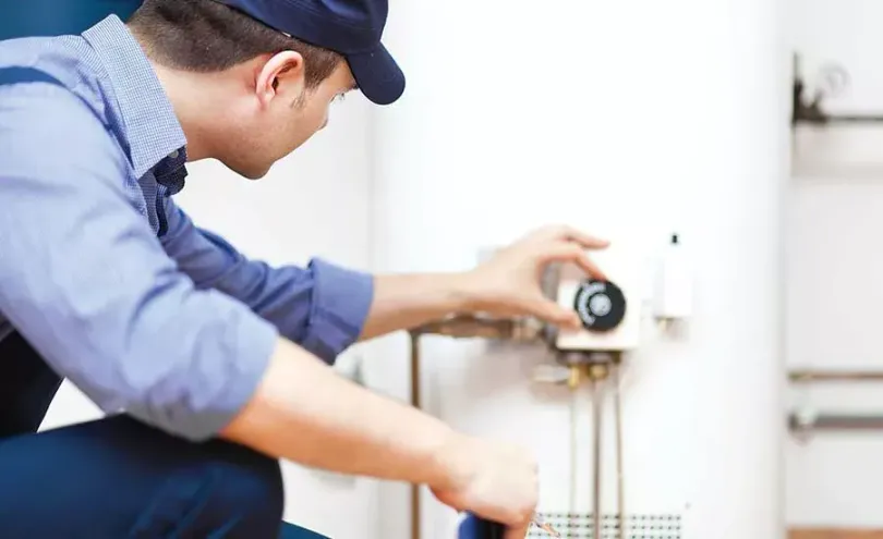 A professional in uniform adjusting the temperature dial on a white water heater.