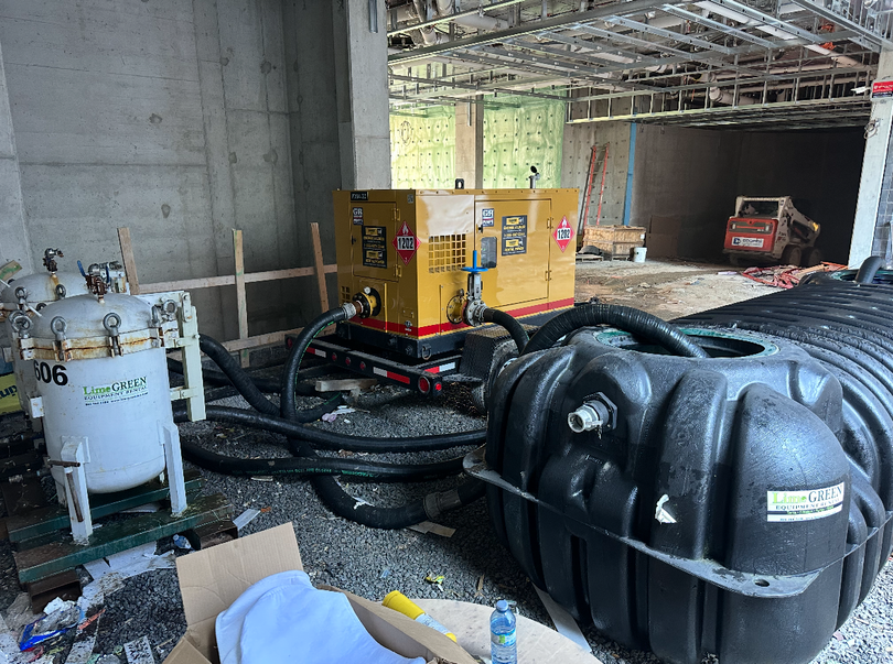 Two technicians in hard hats examine industrial machinery together in a mechanical room, one holding a clipboard.
