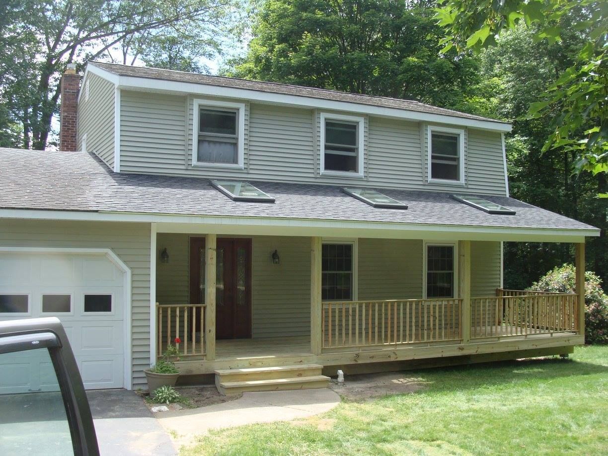Light green two-story house with a wraparound porch, garage, and three upper-level windows.