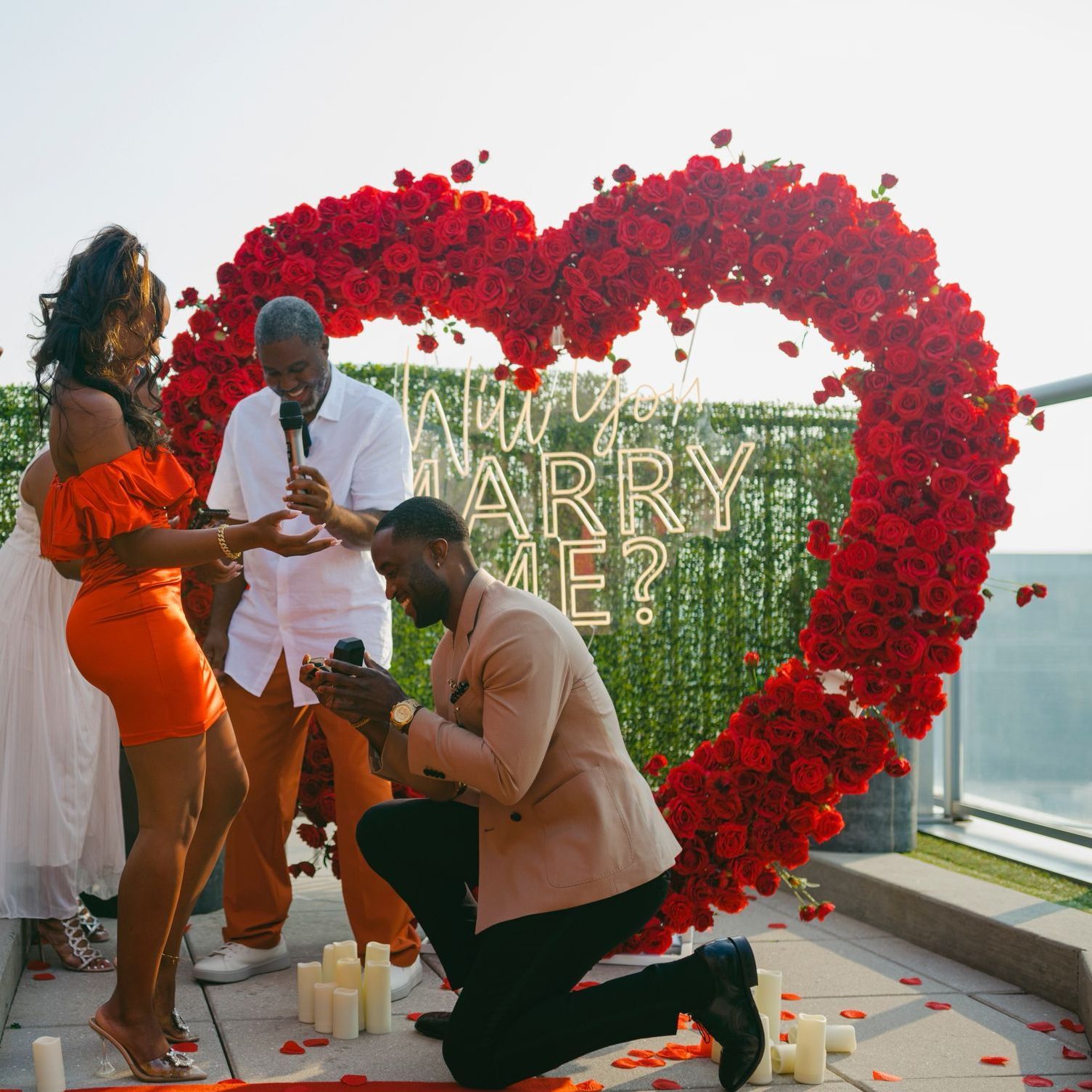 A man is proposing in front of a heart shaped wall that says marry me