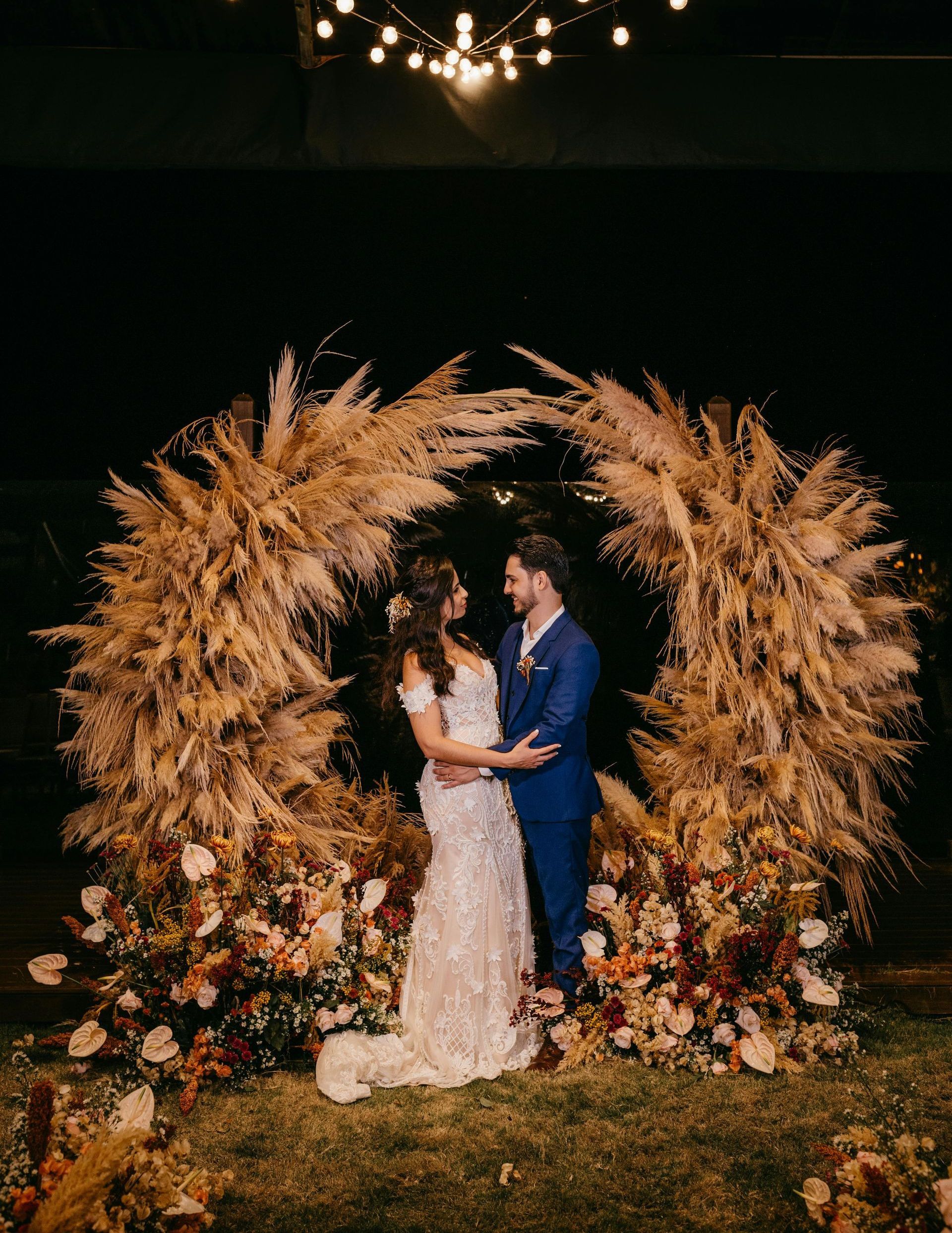 A bride and groom are standing in front of a fall floral arch.