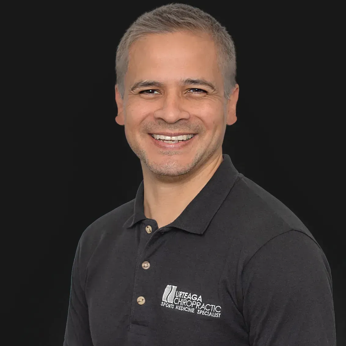 Smiling man in a black polo shirt with a logo. Against a black background.