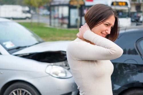 Woman clutching neck in pain next to damaged cars after car accident.