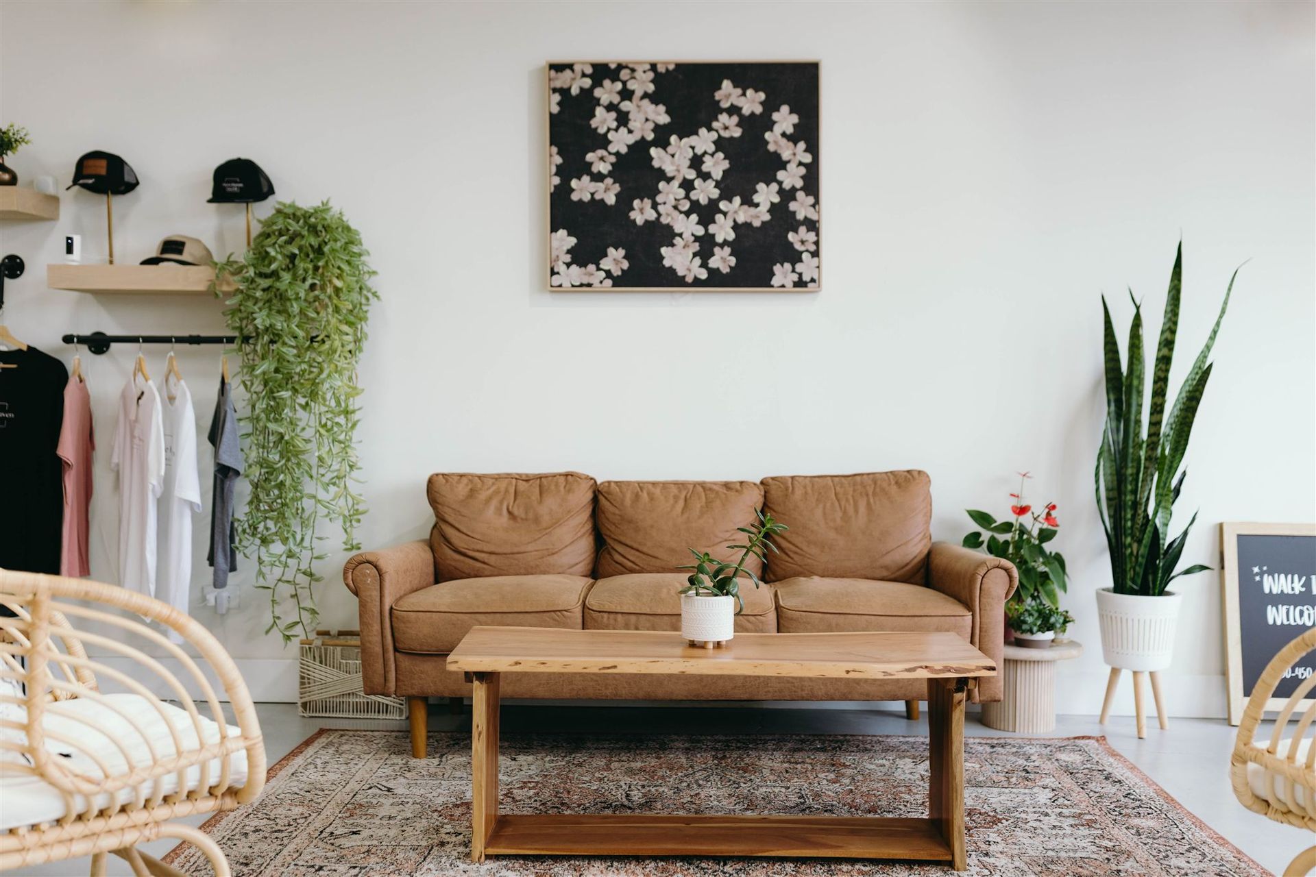 Cozy living room with tan sofa, coffee table, rug, plants, and wall art against white walls