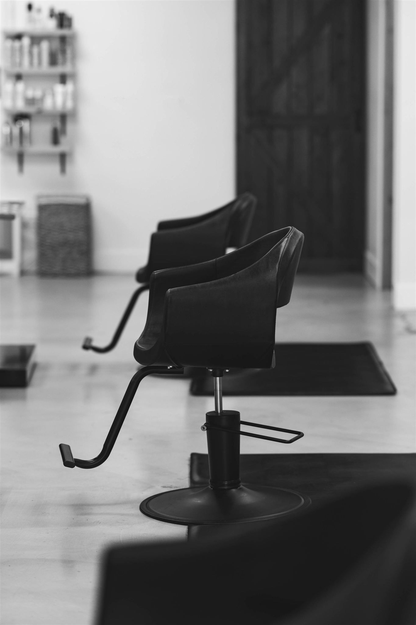 A woman in a black dress is sitting in a black chair in a salon.