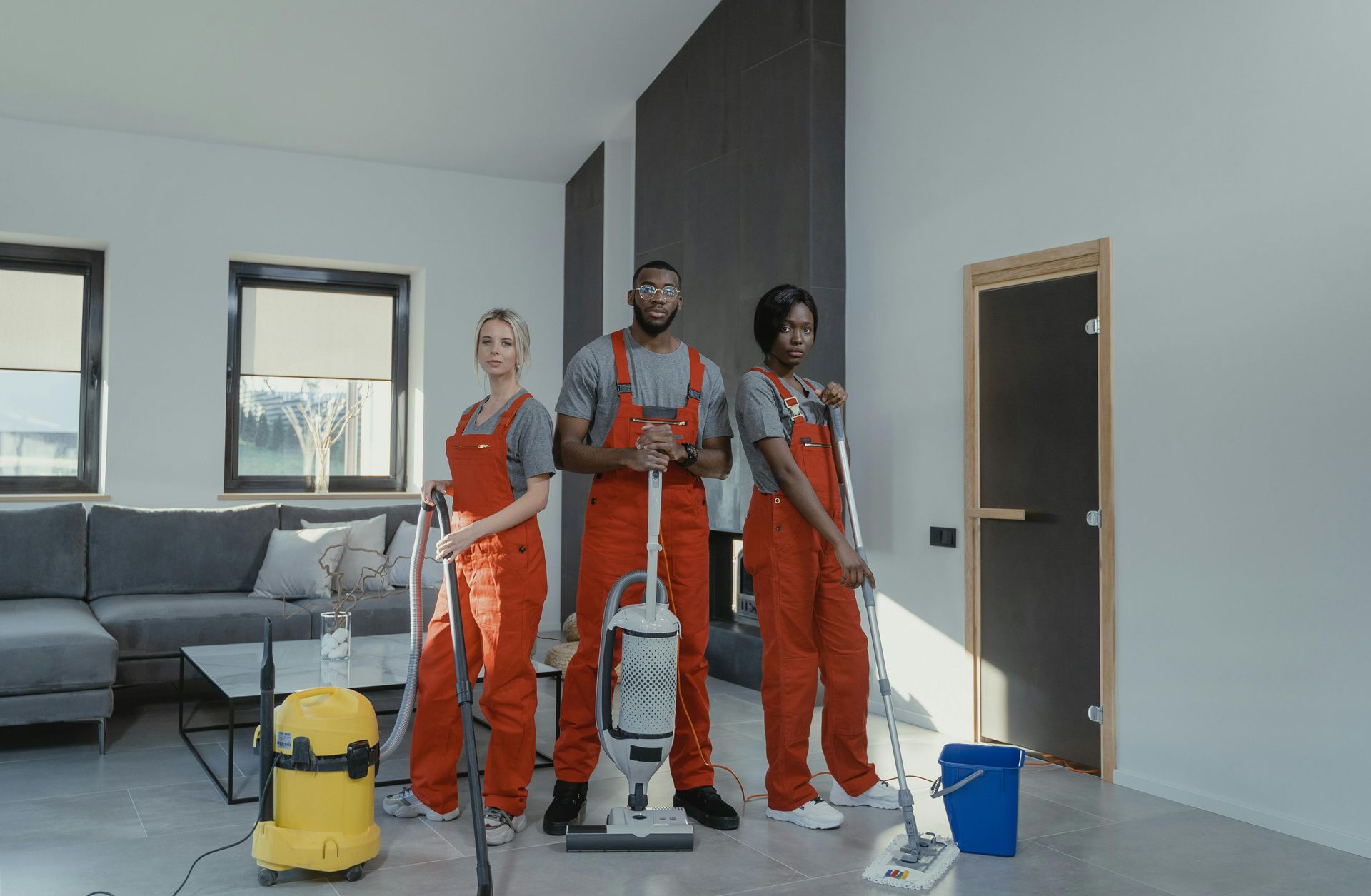 Three people in orange jumpsuits hold cleaning supplies in a modern room.