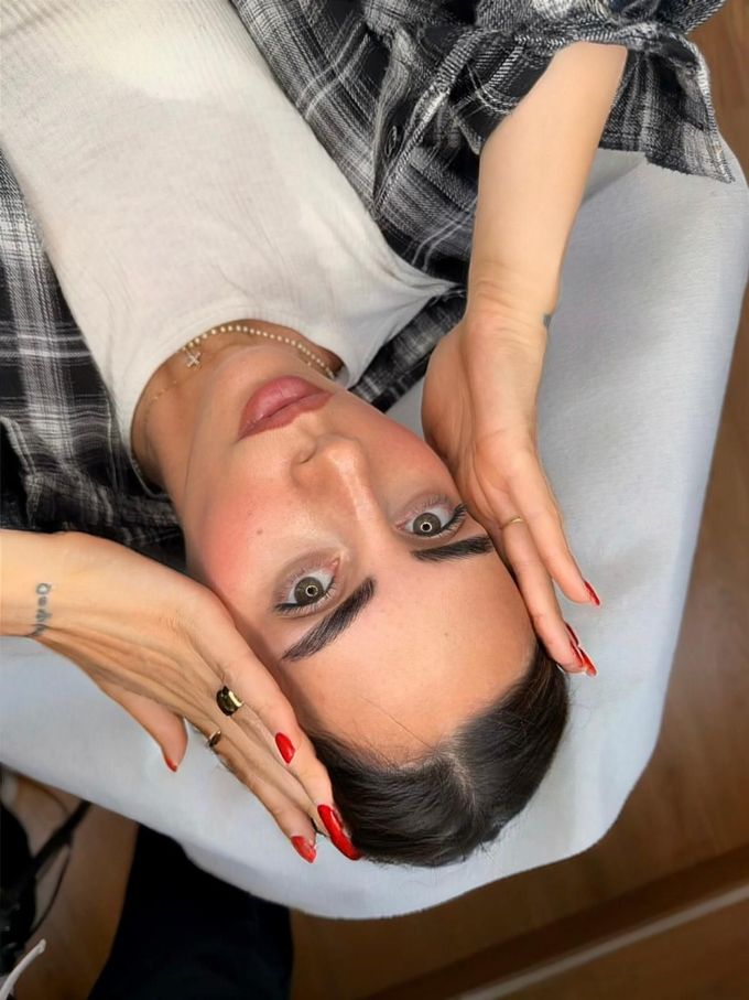 Primo piano di un occhio marrone e di un sopracciglio folto e scuro. L'occhio presenta mascara e un riflesso luminoso.