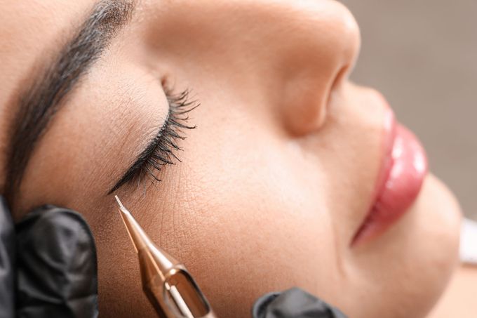 Tatuaggio con eyeliner applicato sull'occhio chiuso di una persona: eyeliner nero, ago dorato, guanto nero.