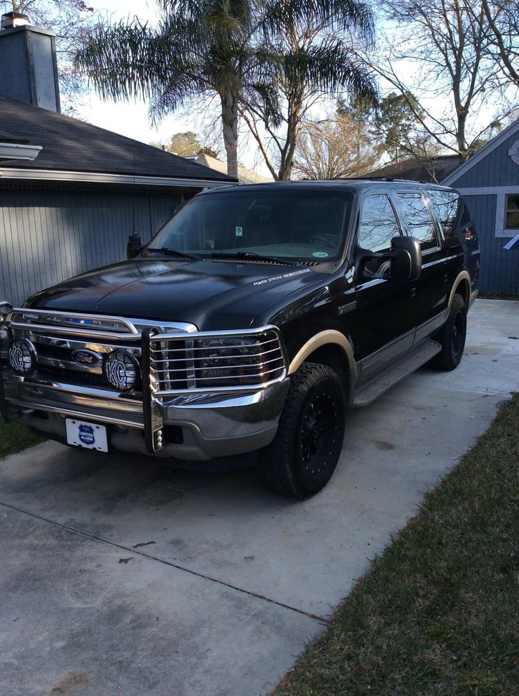 Black SUV parked in a driveway outside a house, with a chrome grille guard.